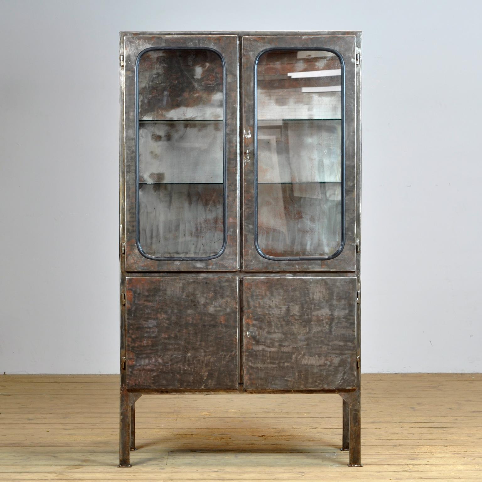 This medical cabinet was designed in the 1970s and was produced circa 1975 in hungary. It is made from iron and glass, which is held by a black rubber strip. The item has been stripped from its paint and treated for rust. The cabinet features two