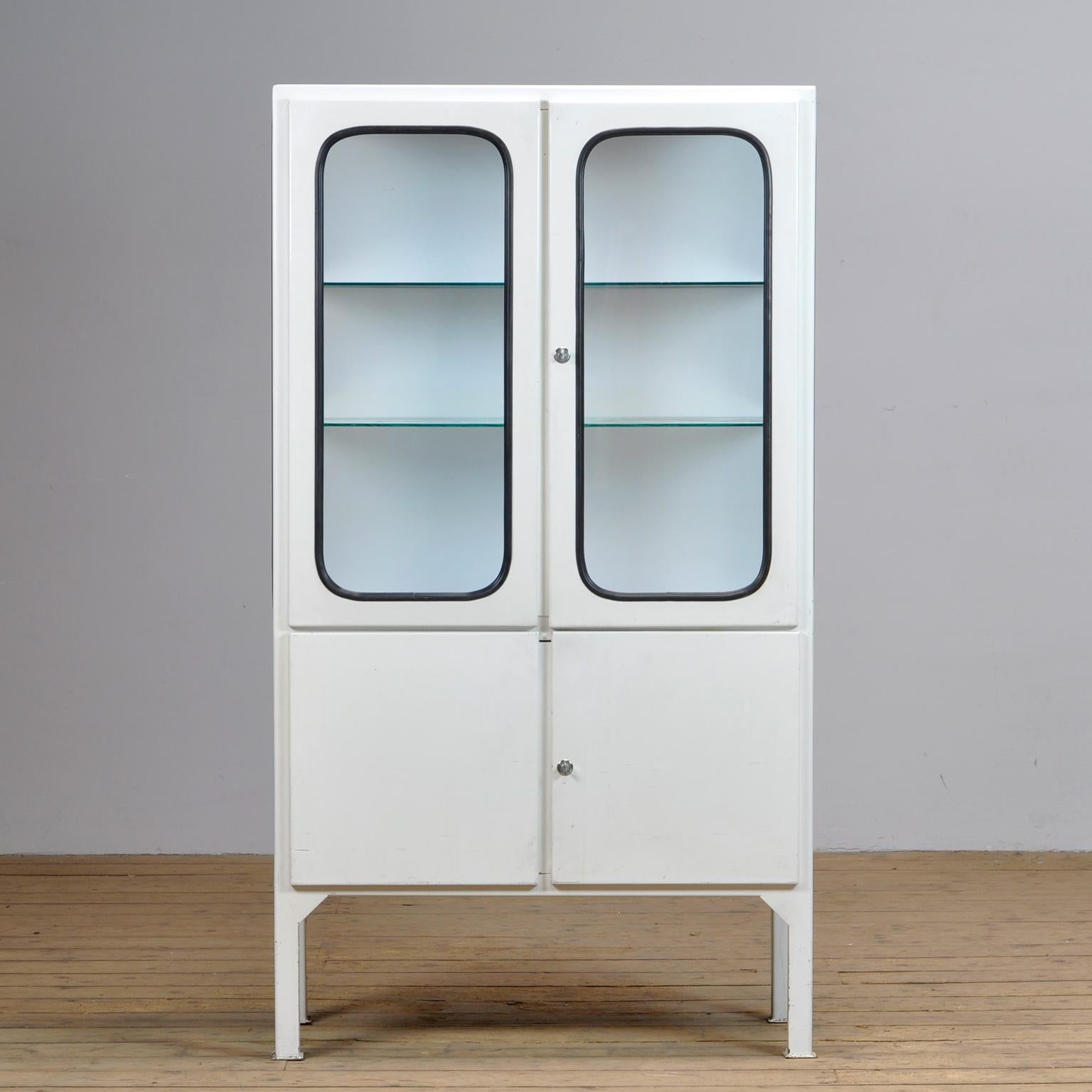 This medicine cabinet was designed in the 1970s and was produced circa 1975 in hungary. It is made from iron and antique glass, and the glass is held by a black rubber strip. The cabinet features two adjustable glass shelves and functioning