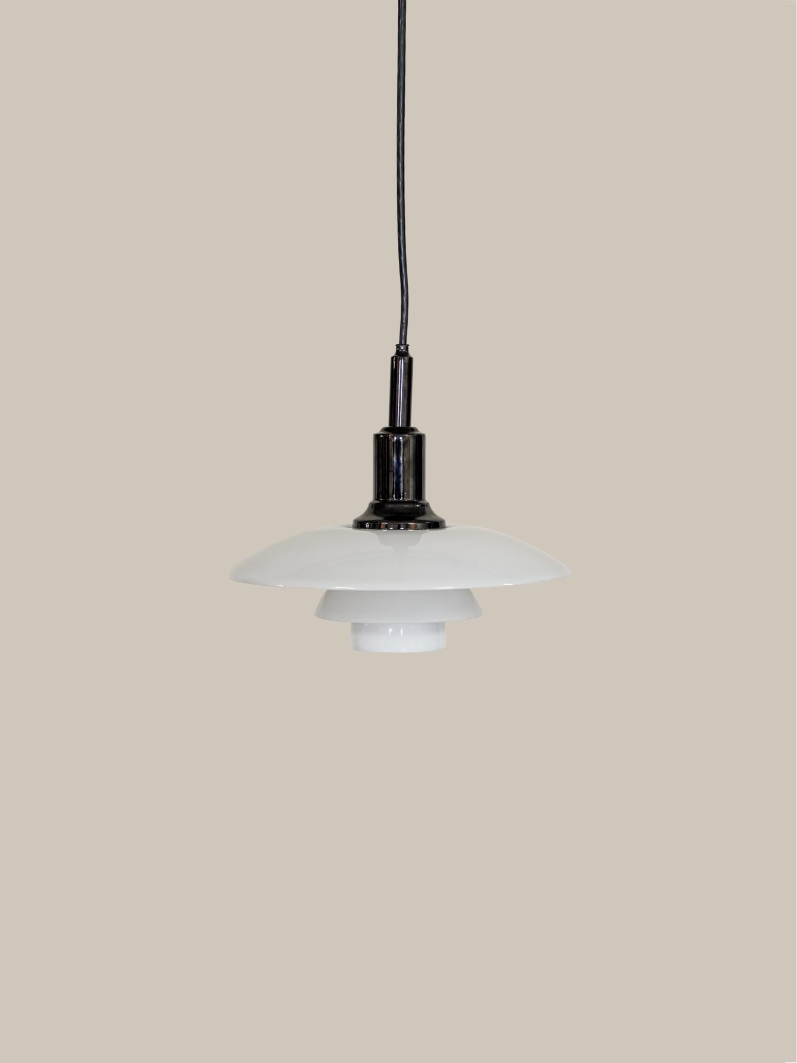 With its white, shallow-dome-shaped glass shade and black metal socket assembly, this pendant light is a stellar example of minimalist design. The form and scale are a perfect choice for direct area lighting in a mid-century dining room or kitchen.