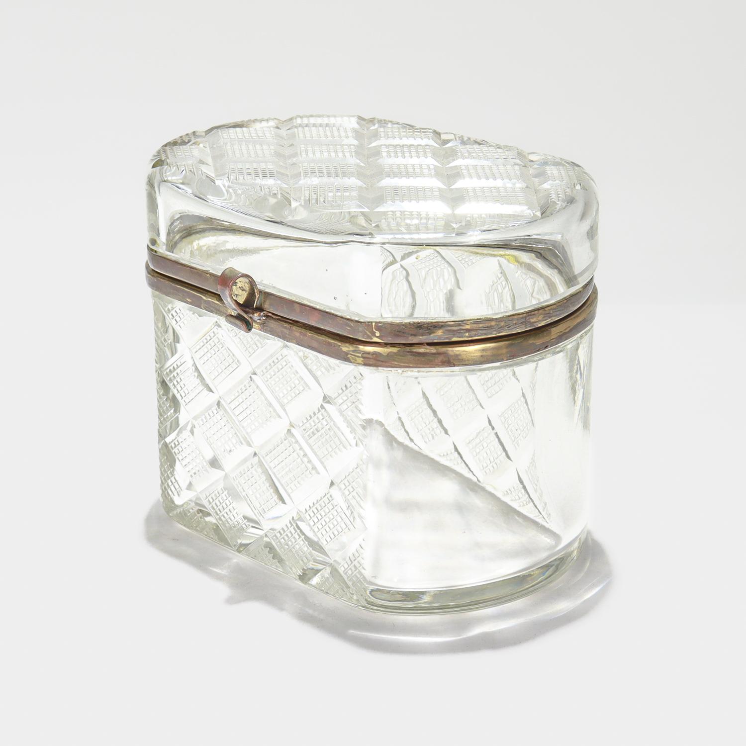 Un cofre o caja de mesa de cristal fino.

De forma oval aplanada.

Con montura de metal dorado y decoración de cristal tallado en forma de fresa en la parte superior, delantera y trasera. 

Sencillamente, ¡una caja estupenda!

Date:
siglo XX

Estado
