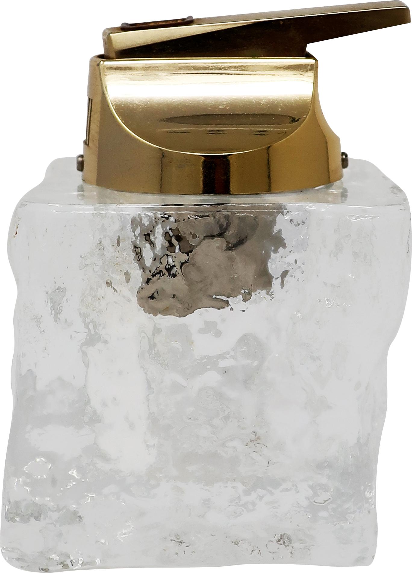 A vintage table lighter with brass colored insert and glass base reminiscent of an ice cube. Hefty yet elegant and will fit beautifully in a Mid-Century Modern or contemporary designed home or office. In excellent vintage condition with no maker’s