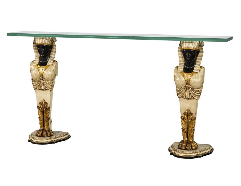 This Egyptian console table is a real piece of history. Comprised of a thick glass slab sitting atop two hand carved, hand painted, and gilded Egyptian Pharaoh sculpture supports. A truly striking and unique piece perfect for a well-traveled home.