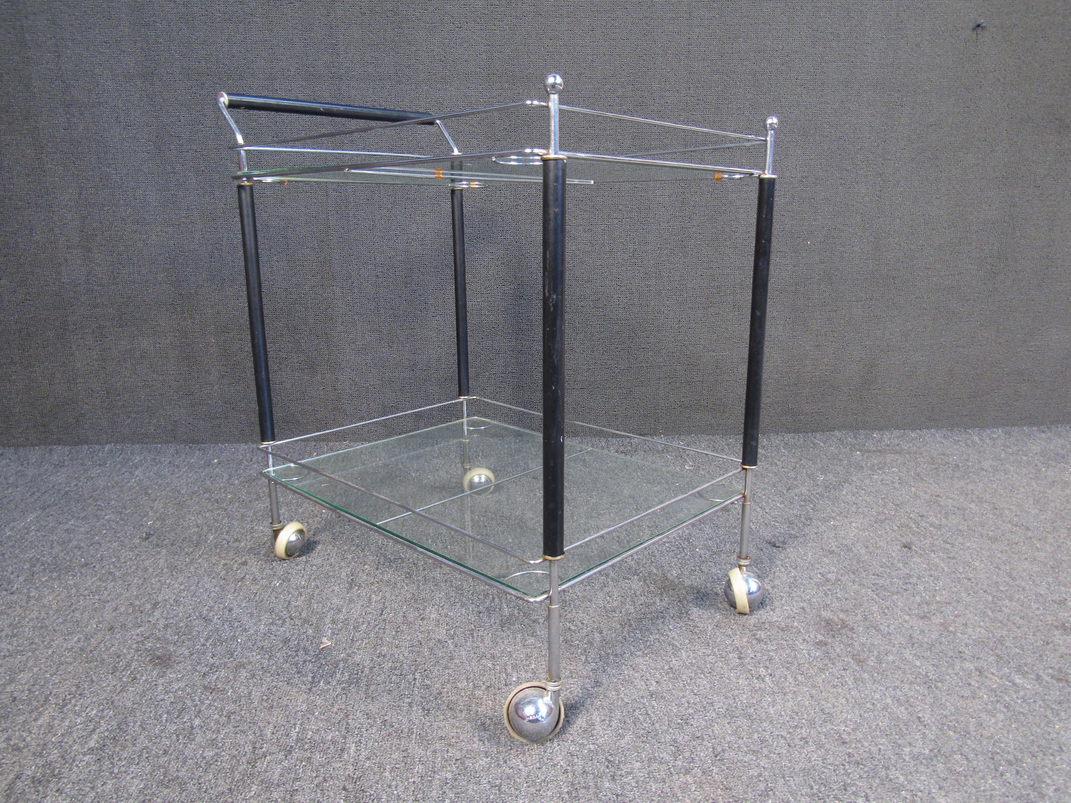 This gorgeous vintage modern serving cart features stylish sculpted metal fixtures and unique rods around each shelf. Sleek design offers plenty of room for items on its two glass shelves. This elegant mid-century piece has unusual metal wheels