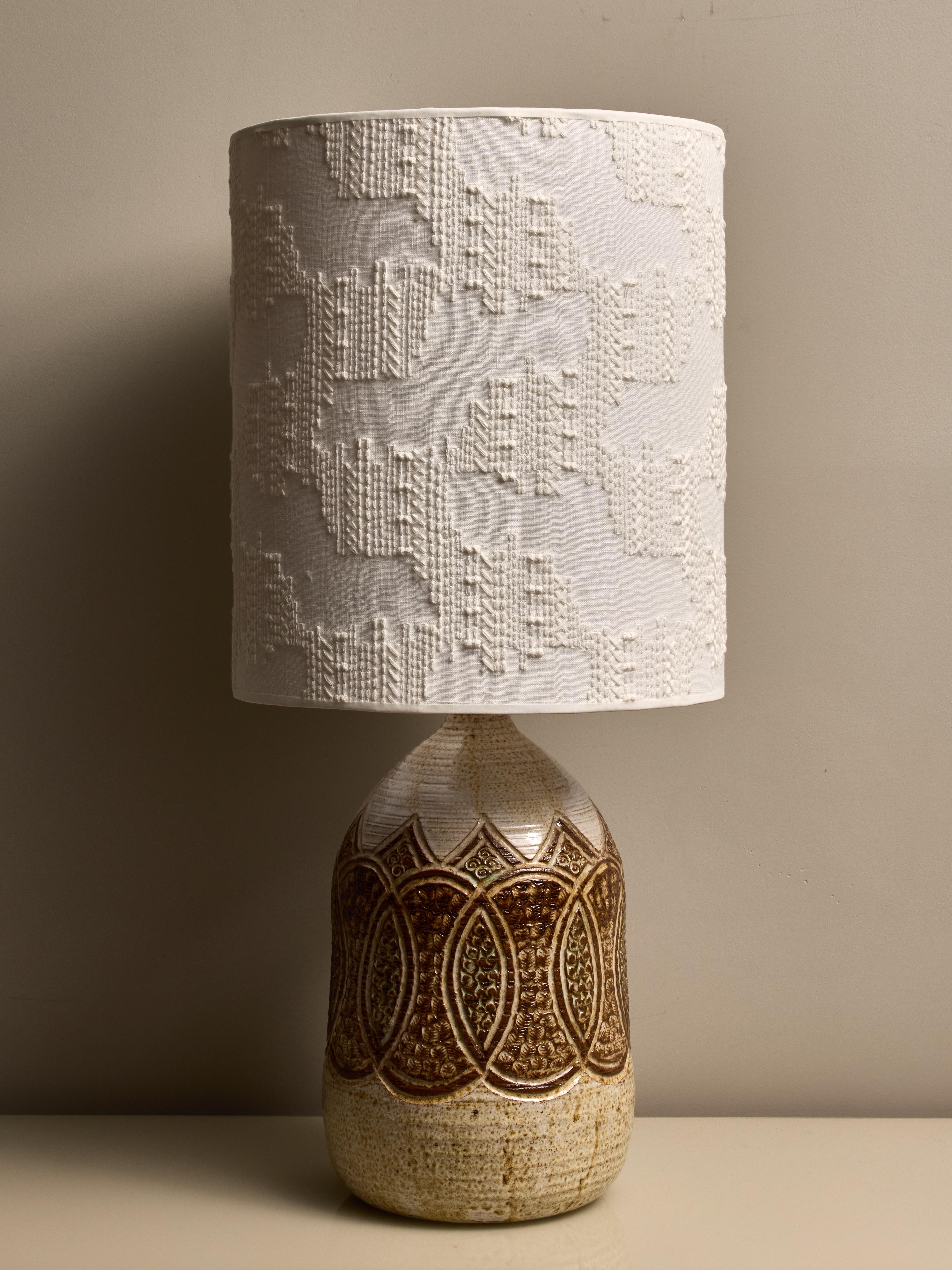 Eine Tischlampe aus glasierter Keramik mit beigen und braunen Mustern wird vorgestellt. Sie verfügt über einen zeitgenössischen Lampenschirm und ist am Sockel mit der handschriftlichen Provenienz 
