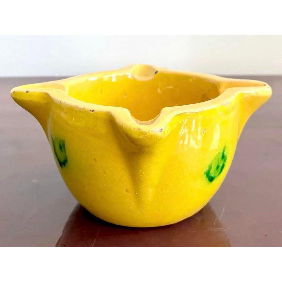 Este cuenco rústico de cerámica amarilla rebosa encanto mediterráneo. El brillante vidriado es rico en rayos de sol, con motas verdes que parecen casi hojas de olivo flotando por sus lados. Su borde irregular en forma de pétalo y su forma modelada a