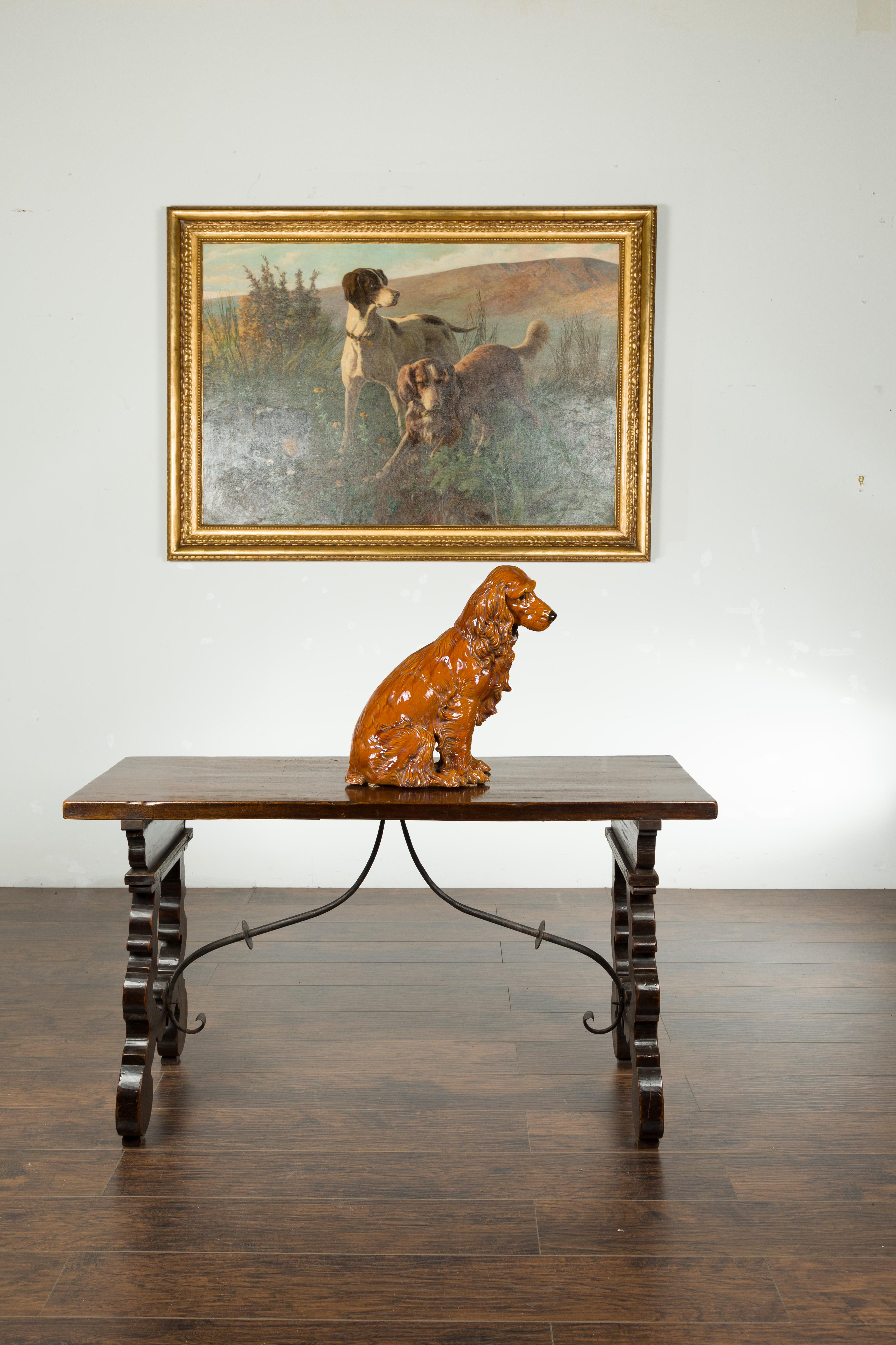 A vintage glazed terracotta dog sculpture from the mid 20th century, depicting a sitting cocker spaniel. Created during the midcentury period, this glazed terracotta piece depicts a cocker spaniel sitting obediently on his behind. Tilting his head