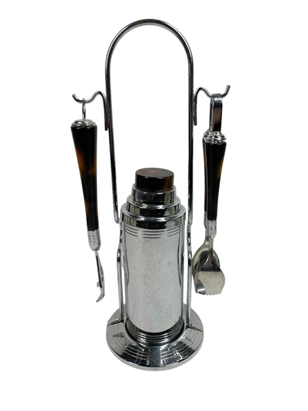 Vintage Glo-Hill chrome and Bakelite cocktail shaker caddy set - chrome with mottled brown faux tortoiseshell Bakelite cylindrical shaker sits in a circular base with a tall arched handle having hooks on either side holding Bakelite handled tong on