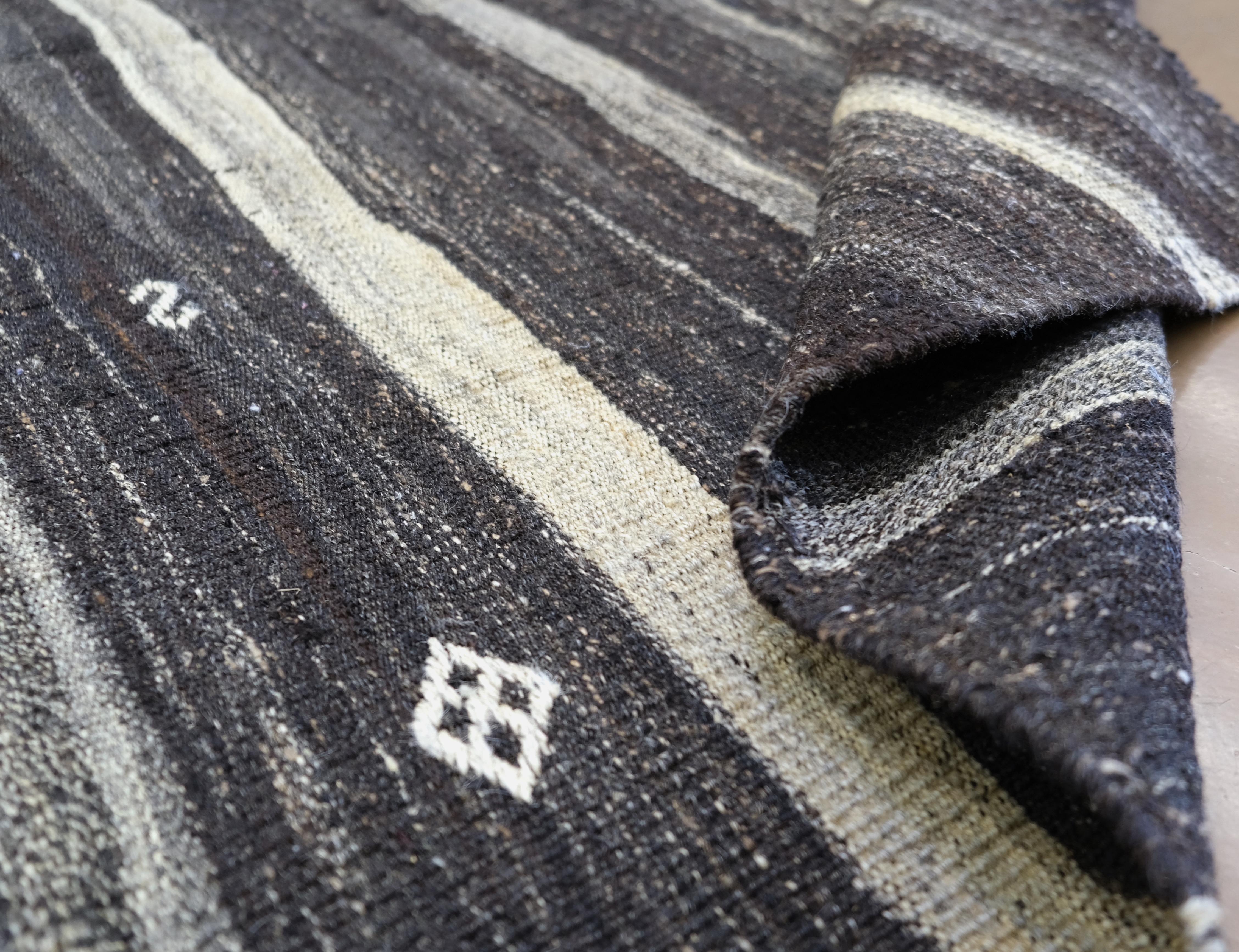Introduci un tocco autentico di eredità turca nei tuoi interni con questo splendido Kilim vintage tessuto a mano, realizzato in pelo di capra naturale. Caratterizzato da un audace motivo a strisce accentuato da motivi tribali tradizionali in