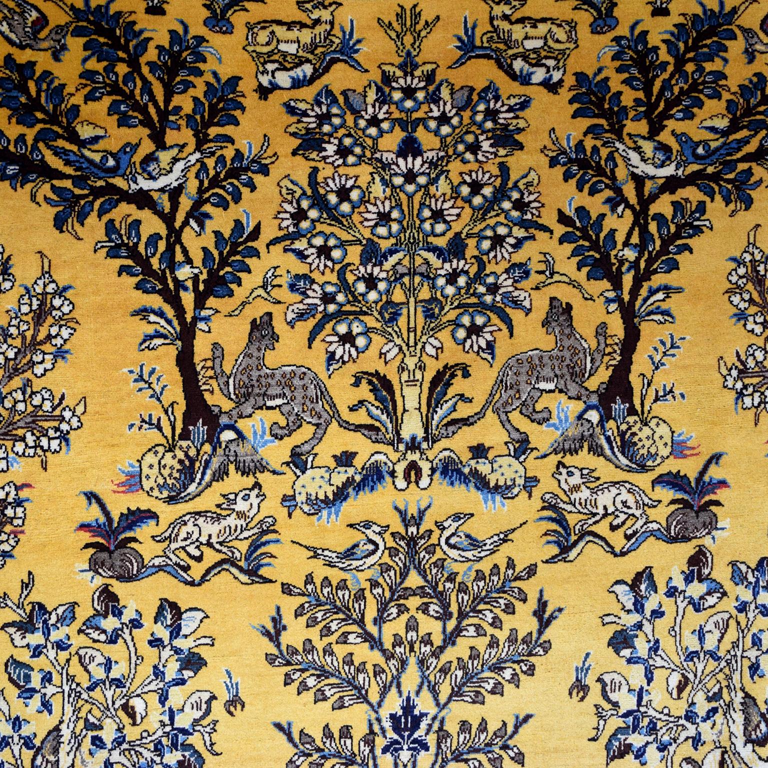 A semi-antique Persian carpet in pure wool dating back to the 1940s, this Ghom carpet features a tree of life design with a surprising golden background and the trees and animals depicted in a deep blue. The carpet is hand knotted in Classic Ghom