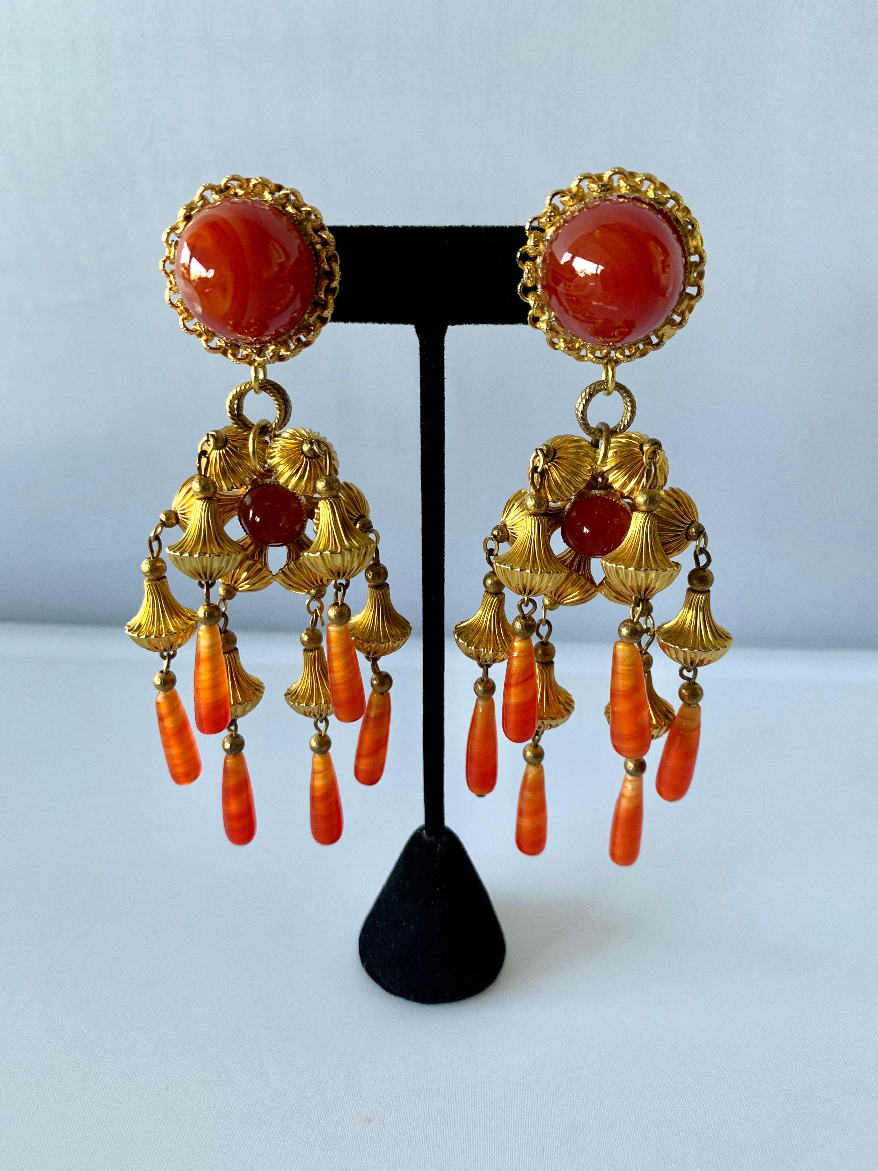 Vintage mid-century statement clip-on earrings comprised out of ornate gilt-metal beads and faux glass carnelian cabochons. The earrings have an oriental design, designed by William de Lillo circa 1969.