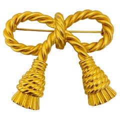 Vieille broche de styliste avec noeud doré et pampille en corde.