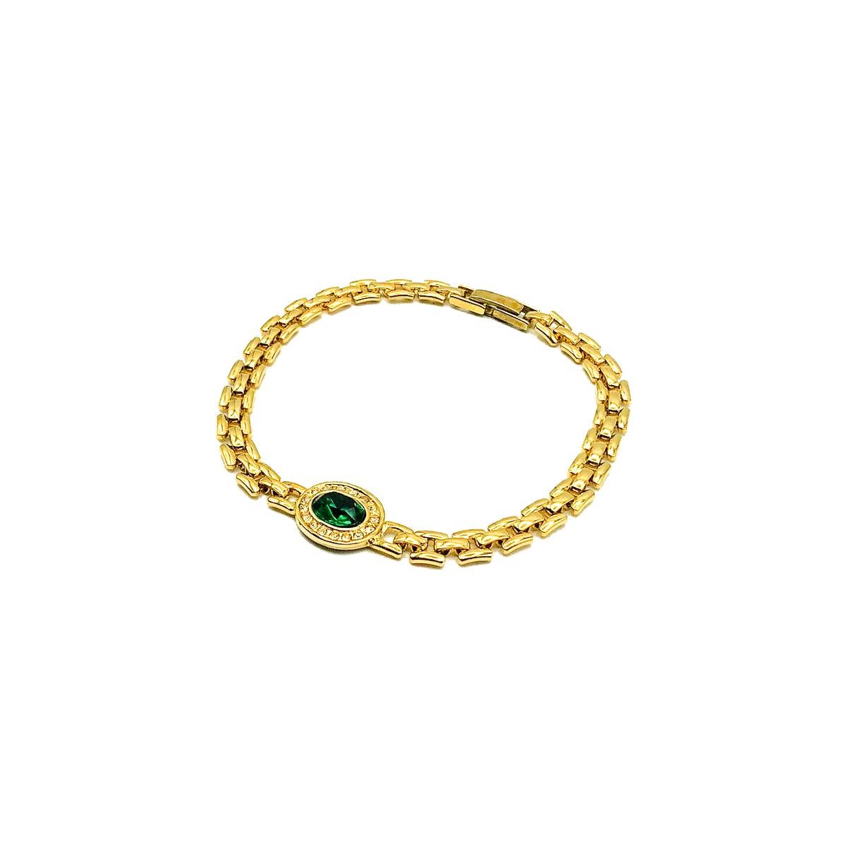 A Vintage Emerald Crystal Bracelet. Featuring a watch strap style chain link with an oval emerald crystal surrounded by clear chaton crystals in the central motif. Crafted in gold plated metal. 19cms. In very good vintage condition. A very pretty