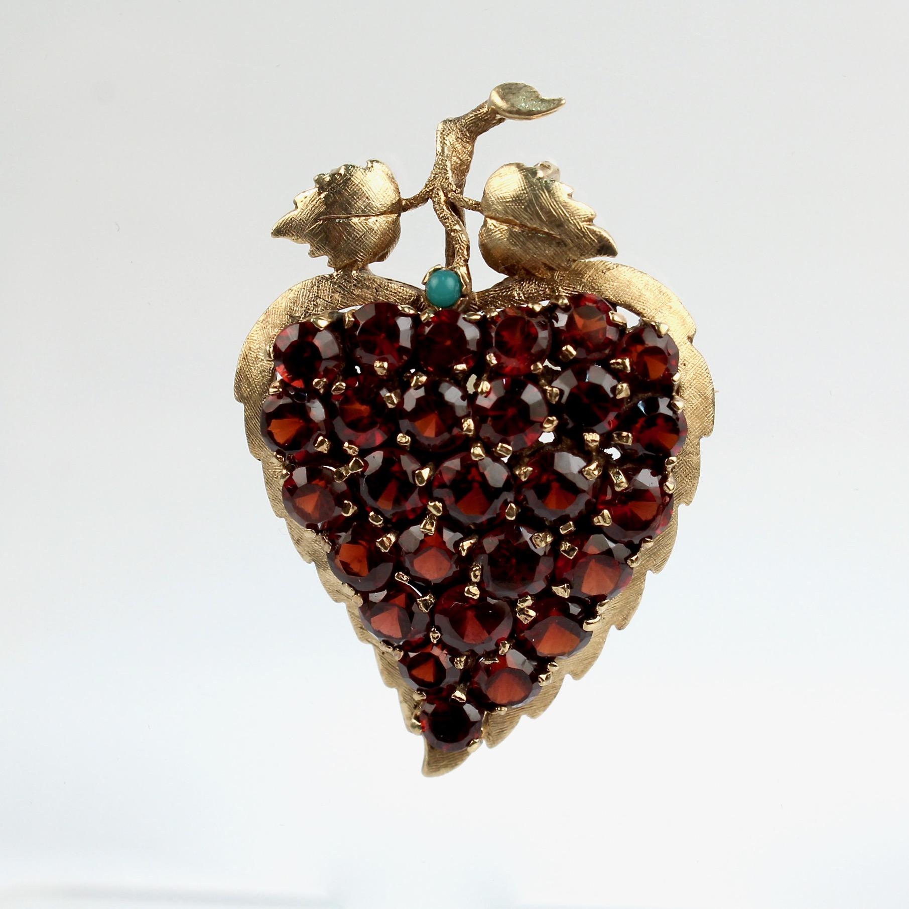 A very fine vintage 10k gold, garnet, and turquoise figural grape cluster brooch. 

In the form of a heart-shaped grape cluster with prong-set garnets as grapes and a figural stem and leaves set with a single small turquoise cabochon.

Simply a