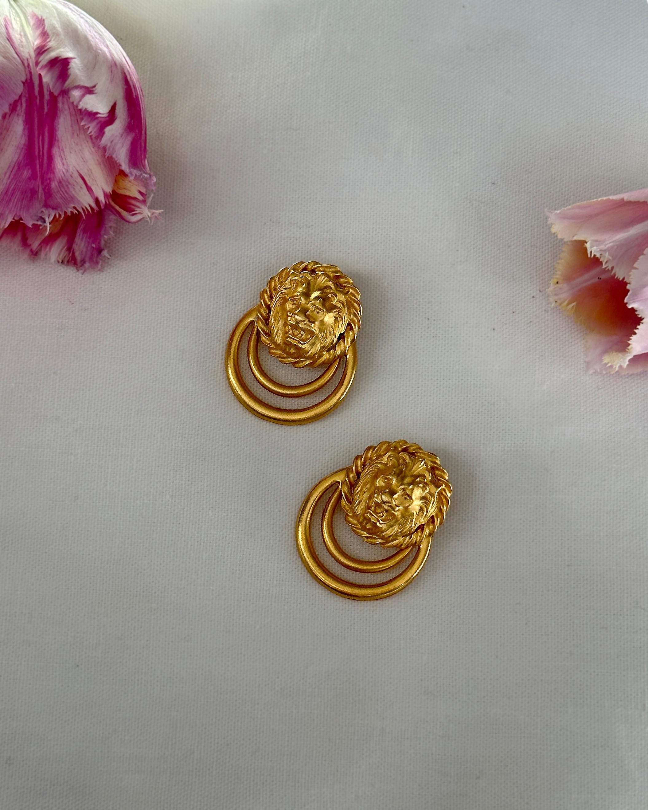 These vintage gold lion doorknocker earrings are giving vintage Versace vibes! They feature a sculptural lion head in rich matte gold, with a swinging circular drop, creating a bit of movement. They are finished with a post back for pierced ears,