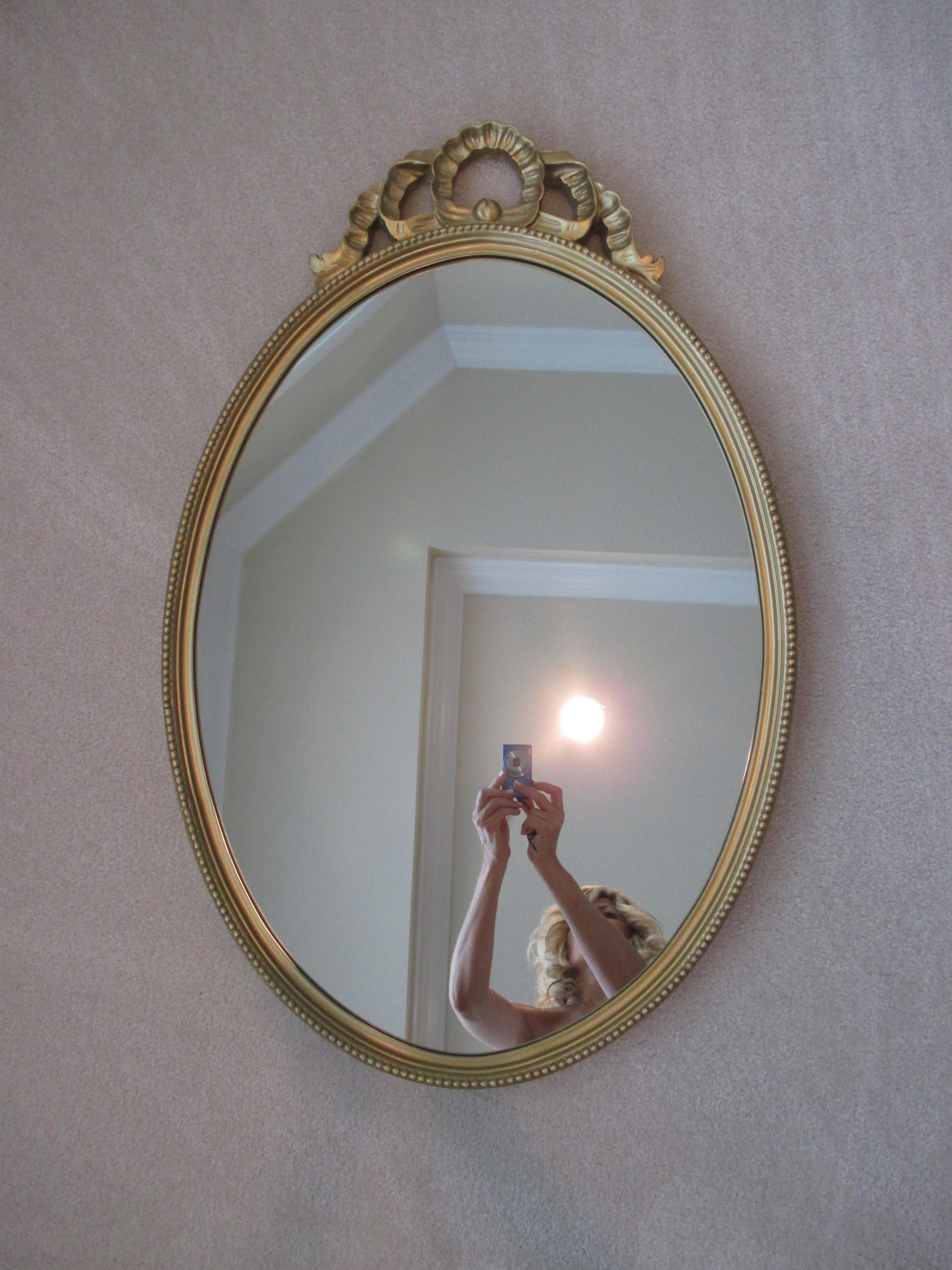Elegant oval shaped gold mirror with ornate detail. Hanging hardware attached.