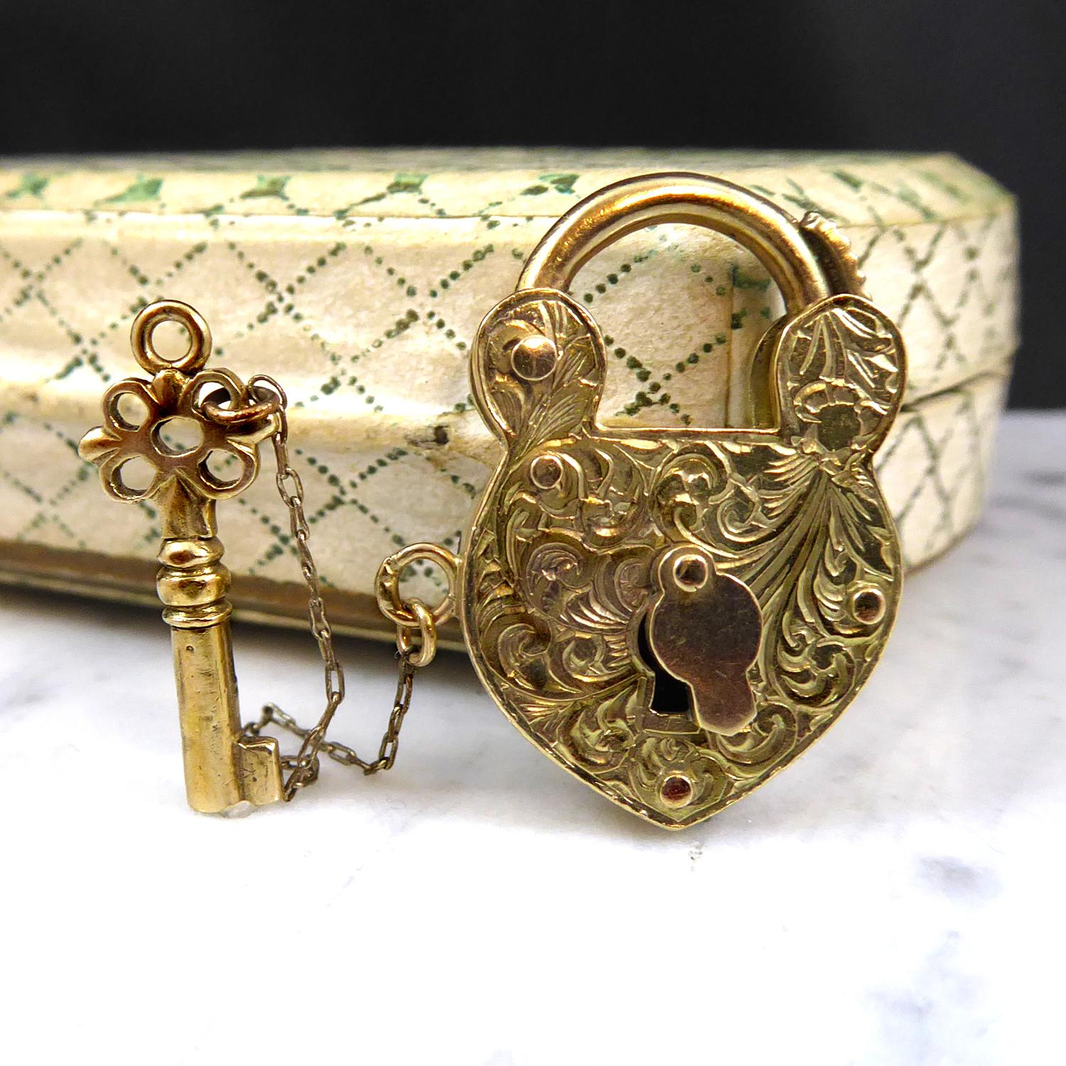 A vintage gold padlock with arabesque engraving to the front and plain polished on the reverse.  The padlock, unusually, is fully-functioning complete with an attached key that can be used to lock the padlock.  The key is attached via a gold chain