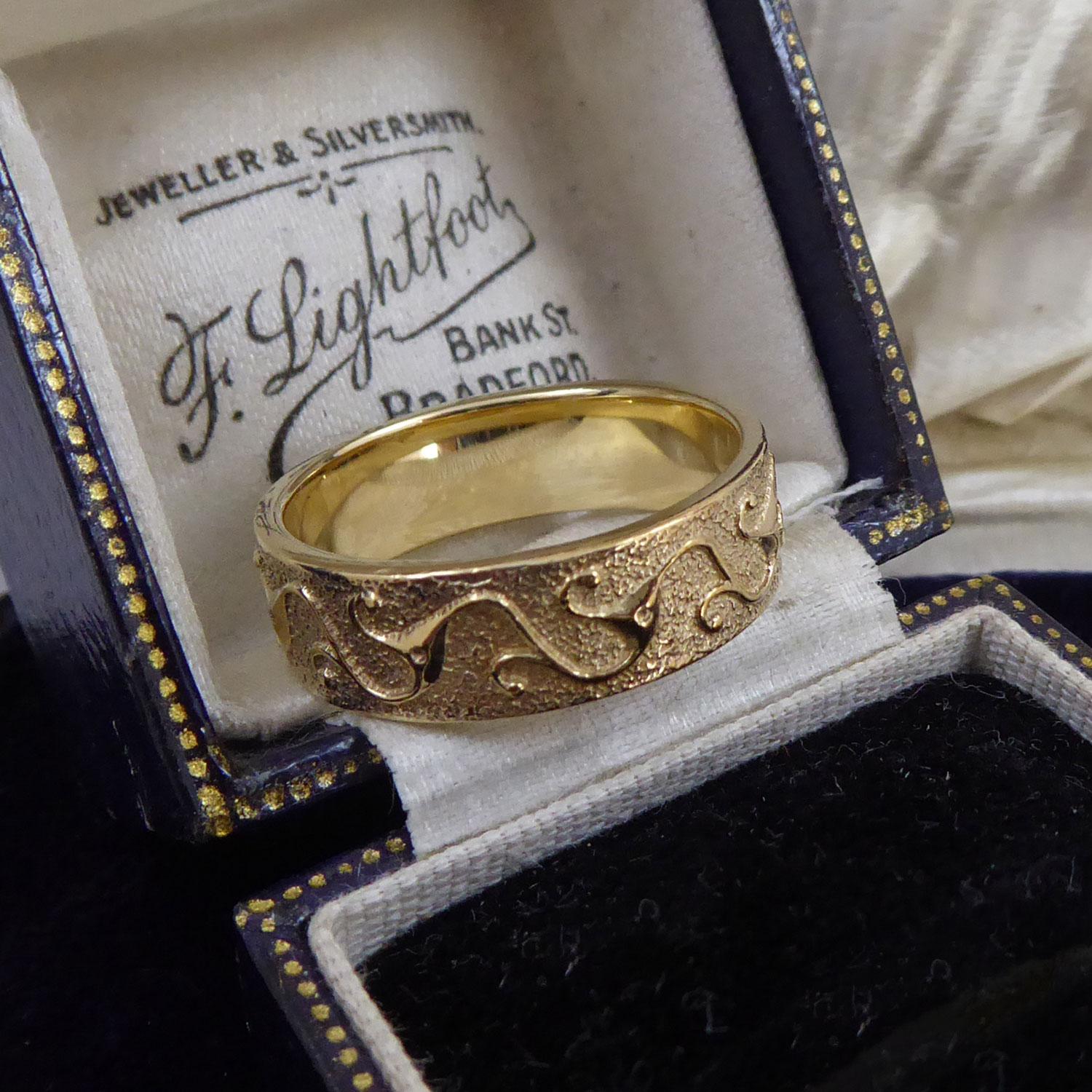 Ein ungewöhnliches Goldband von ziemlich schwerem Kaliber.  Es ist rundherum mit einem polierten, wirbelnden Blatt-/Rankenblattmuster verziert, das von der Art-déco-Ära inspiriert ist.  Der Hintergrund dieses Musters hat eine halbmatte/halbpolierte,