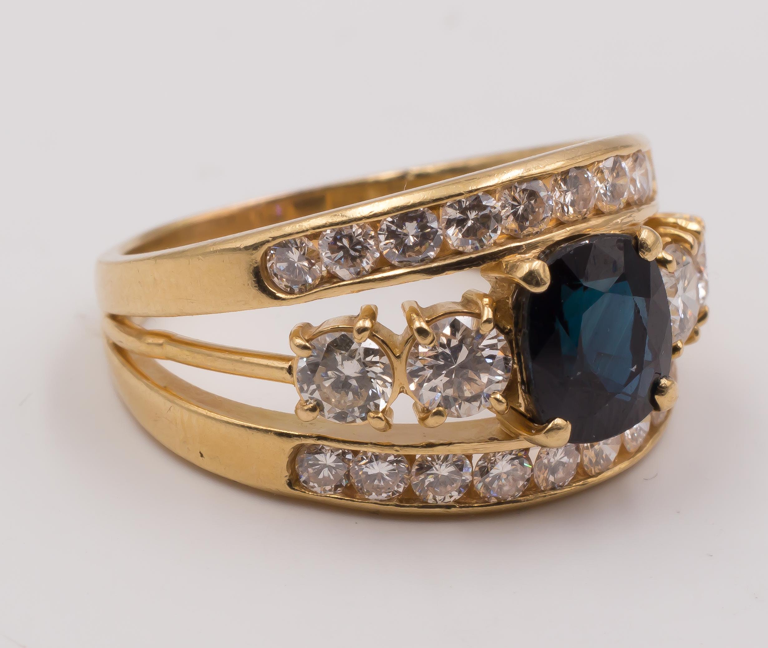 This stunning vintage ring has a beautiful shape, where the shank splits in three bands: the outer ones are each one set with ten round cut diamonds; in the middle of them the central band is decorated with a sapphire, flanked on either side by two