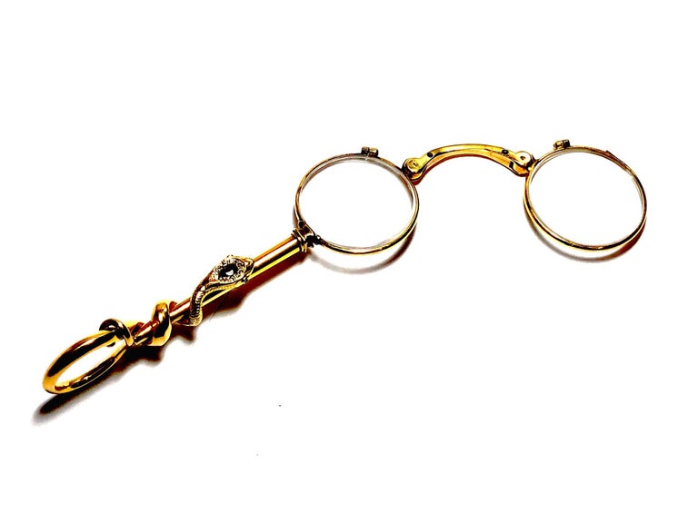 A vintage serpent lorgnette, mounted in 18ct gold, with a snake winding up the handle, the head is set with a pear shaped sapphire, surrounded by old-cut diamonds, with ruby eyes, circa 1940. 
Approximately 120mm long, 42mm at its widest