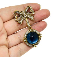 Broche vintage en strass doré avec noeud et pendentif en verre bleu.