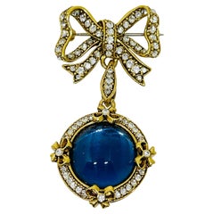 Broche vintage en strass doré avec noeud et pendentif en verre bleu.