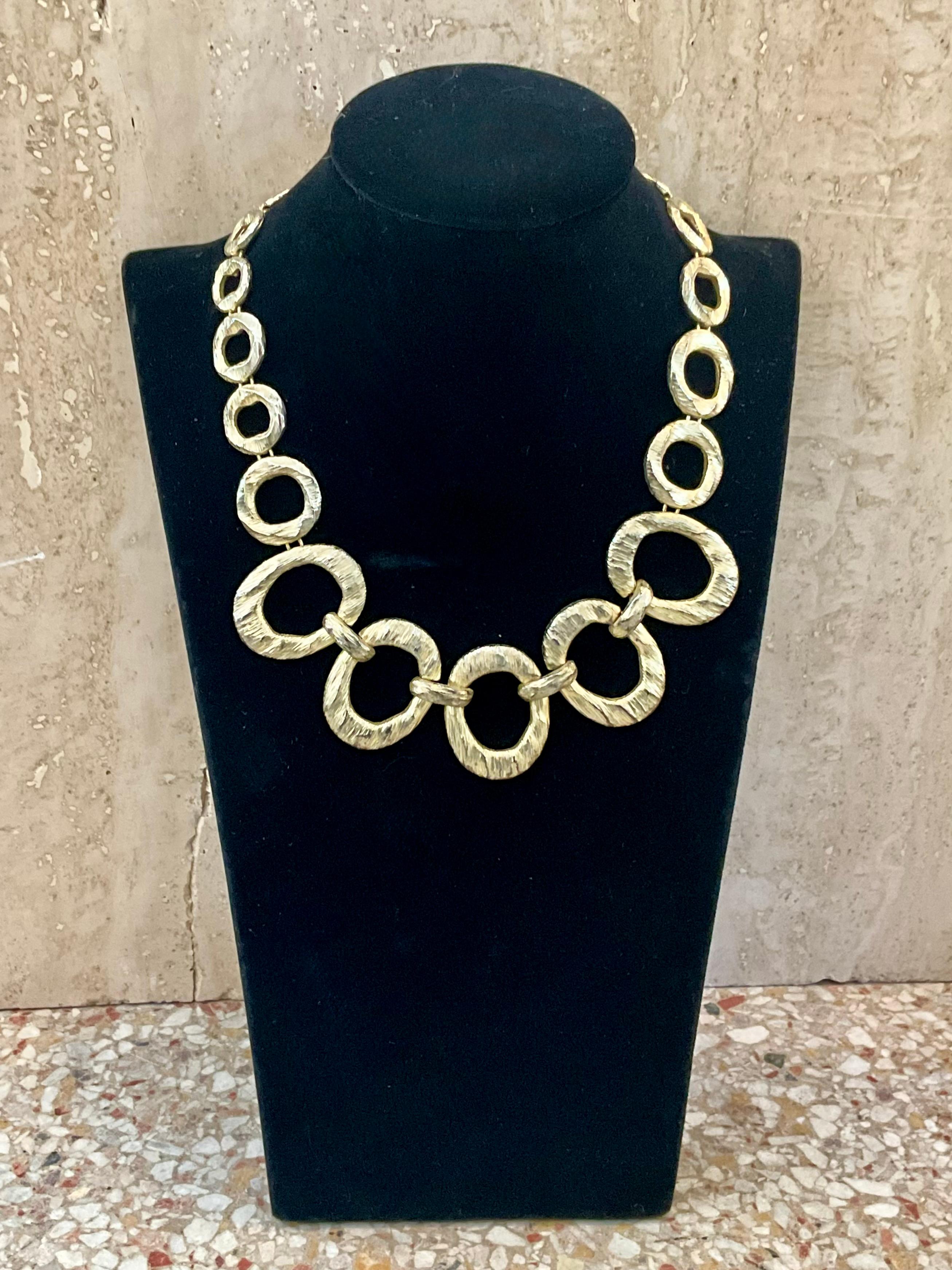La collana Vintage Gold-Toned Hammered Open Circle è un pezzo forte che unisce un'eleganza senza tempo a un design strutturato di ispirazione artigianale. 

L'elemento centrale della collana è un ciondolo a forma di cerchio aperto, che spesso