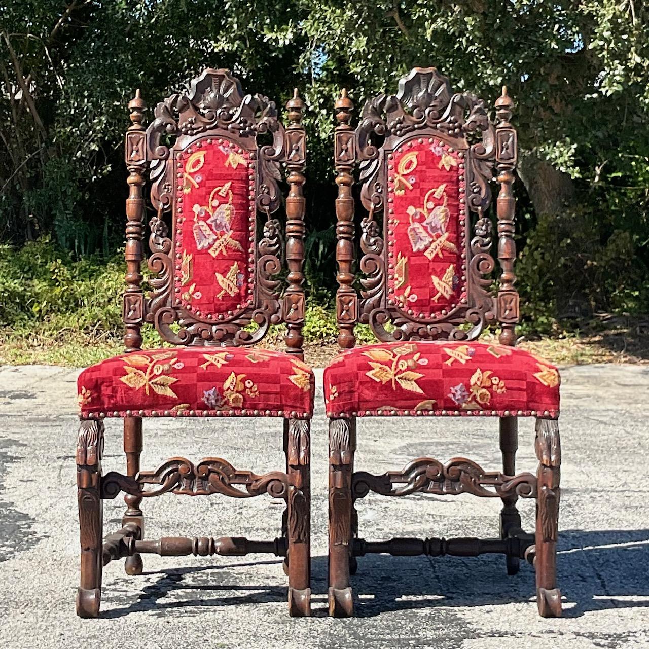 Une superbe paire de chaises de salle à manger gothiques vintage. Magnifique détail sculpté à la main dans une forme gothique classique. Une tapisserie florale rouge brillante en très bon état. Acquis d'une propriété de Palm Beach. 