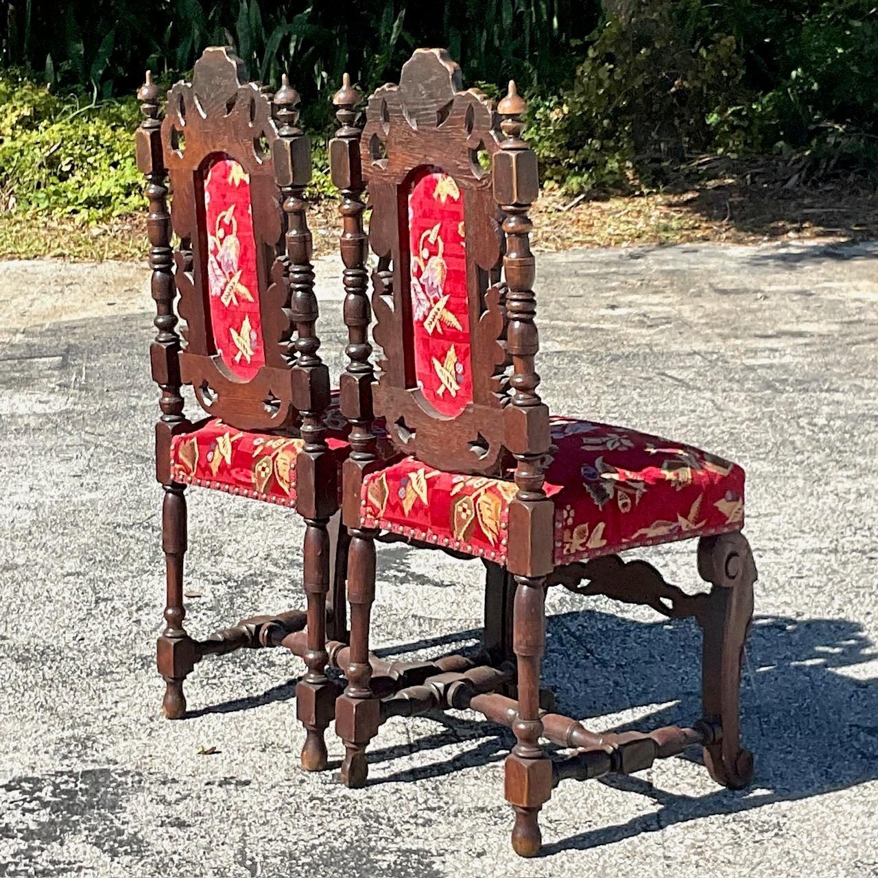 Une superbe paire de chaises de salle à manger gothiques vintage. Magnifique détail sculpté à la main dans une forme gothique classique. Une tapisserie florale rouge brillante en très bon état. Acquis d'une propriété de Palm Beach.
