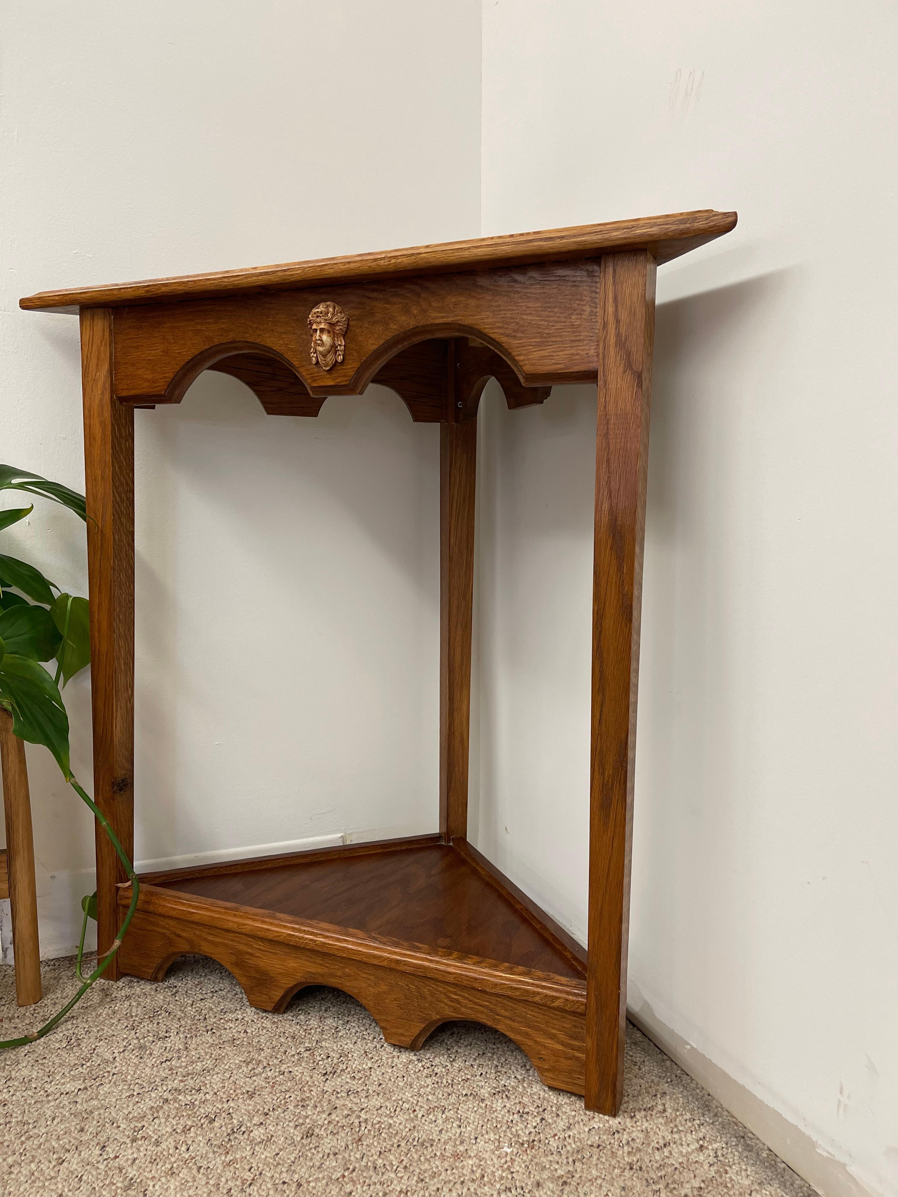 Cette table d'angle vintage présente un style néo-gothique remarquable.  qui se distingue par son tablier festonné et sa forme triangulaire distinctive, conçue pour s'intégrer parfaitement dans un coin. La table présente de magnifiques veines de