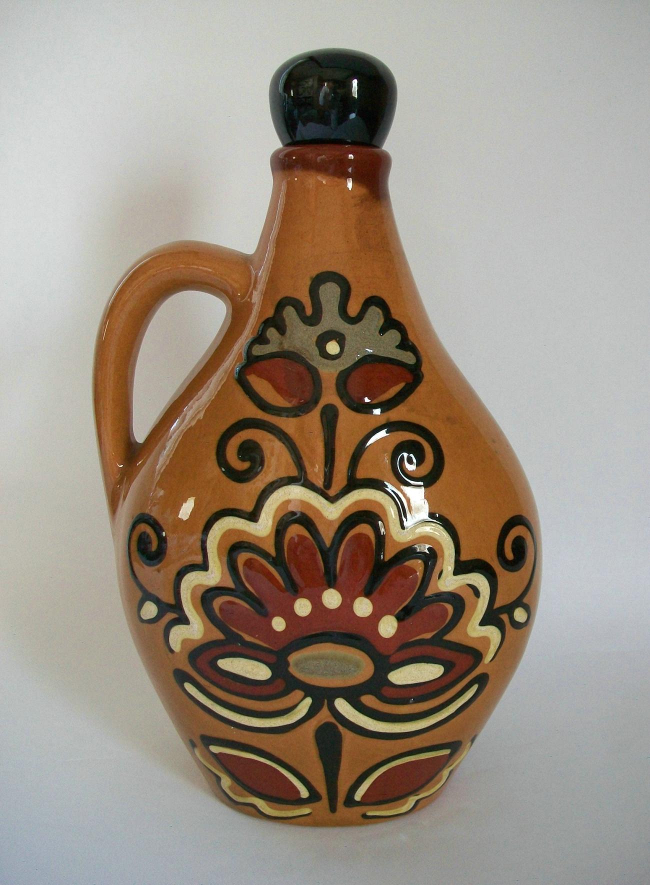 Vintage Gouda folk art pottery jug or decanter with stopper - hand painted stylized floral decoration to the front and back - clear high gloss glaze with slip details - remnants of old factory or retail label to the base - unsigned - Netherlands -