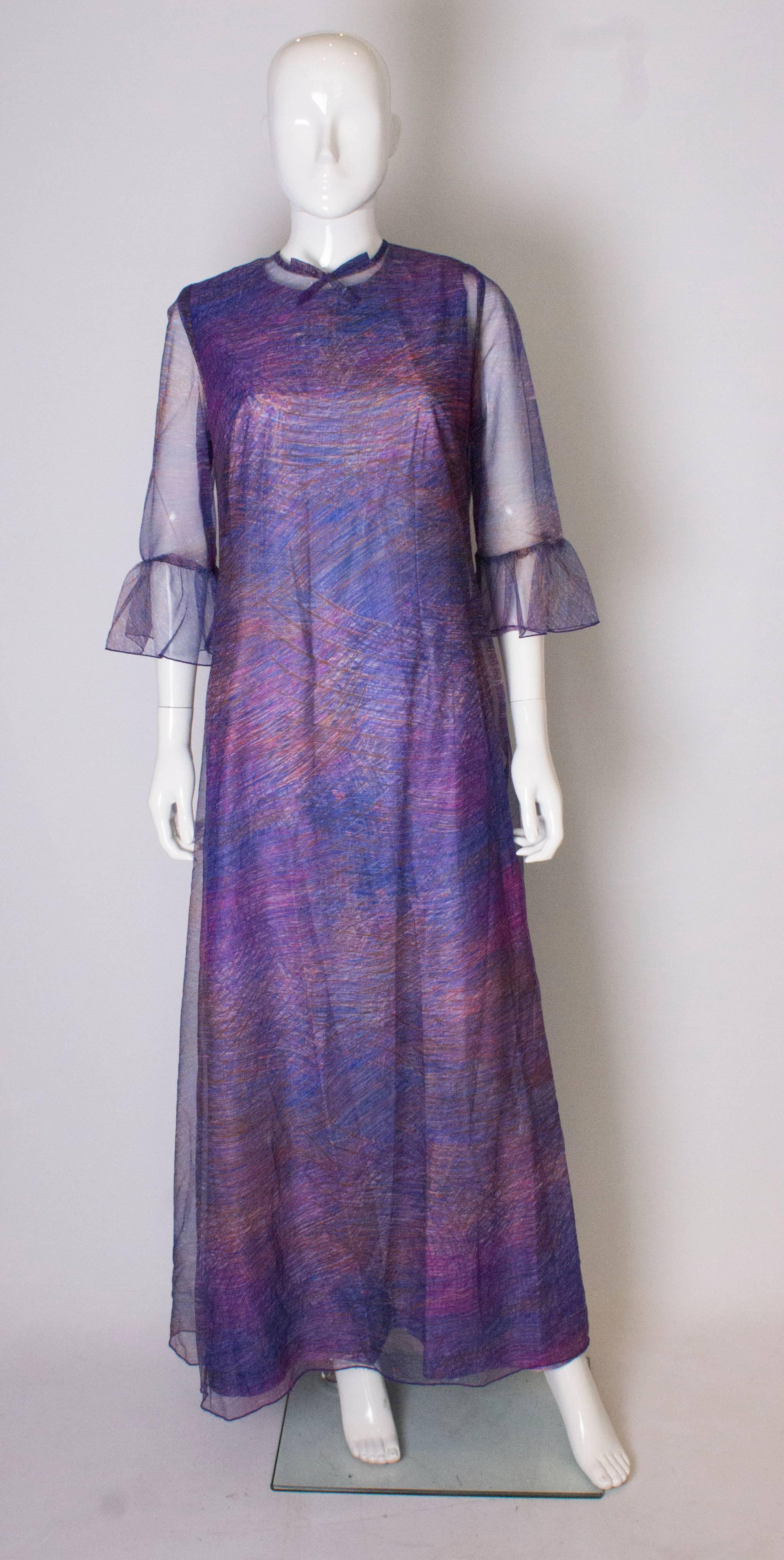 A stunning gown by Clive Byrne, London. The gown has an under dress and an over dress ( both can be worn seperately). The underdress is sleaveless , in a purple,, pink, and orange abstract print. The outer dress has elbow length sleeves with frills