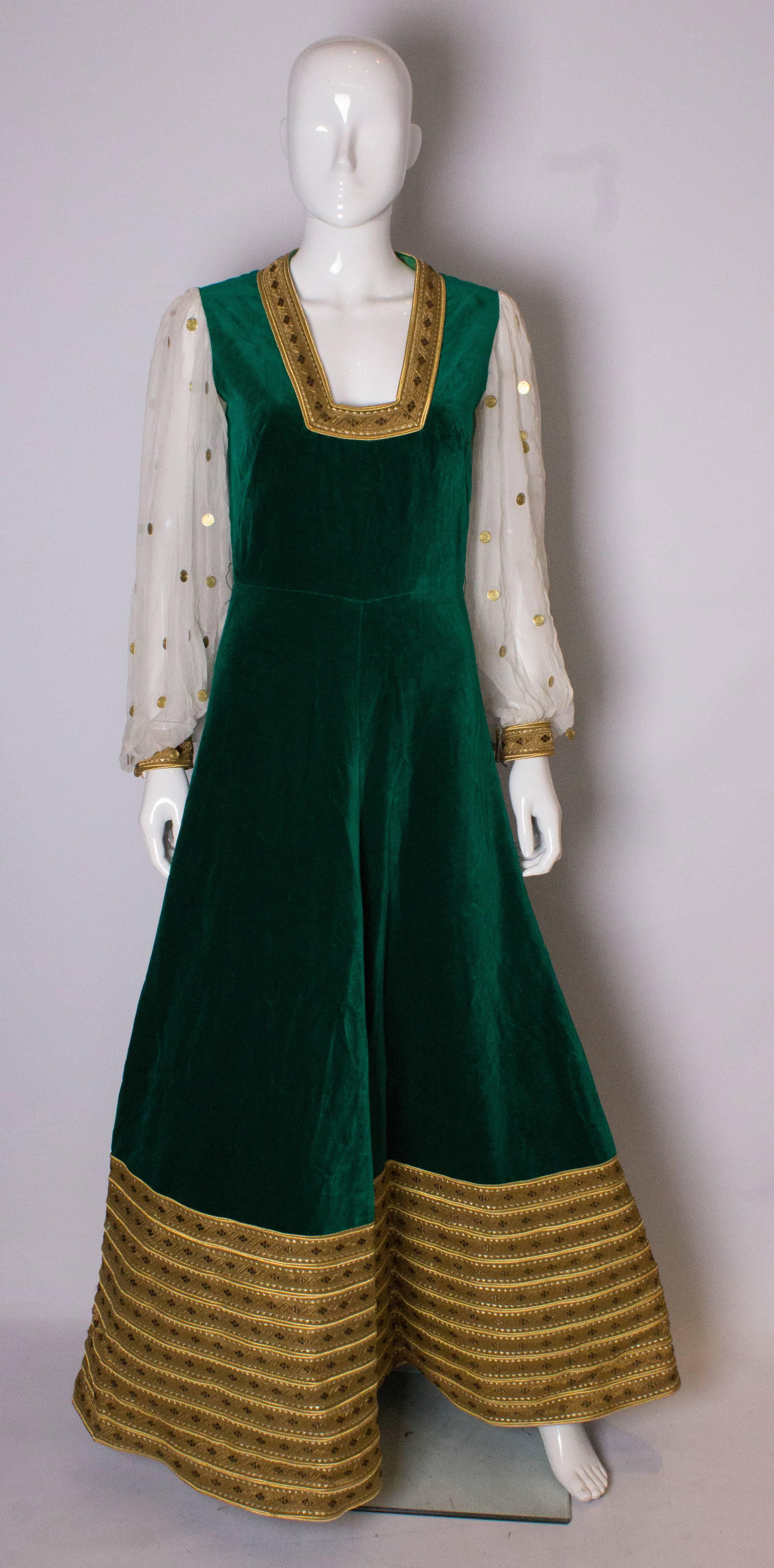 A great gown by Regamus , London . The gown has a boho vibe, in a wonderful green velvet with wide gold trim border at the hem.  The sleeves are chiffon with gold coins attached and have gold cuffs. It is fully lined with a square neckline, anmd