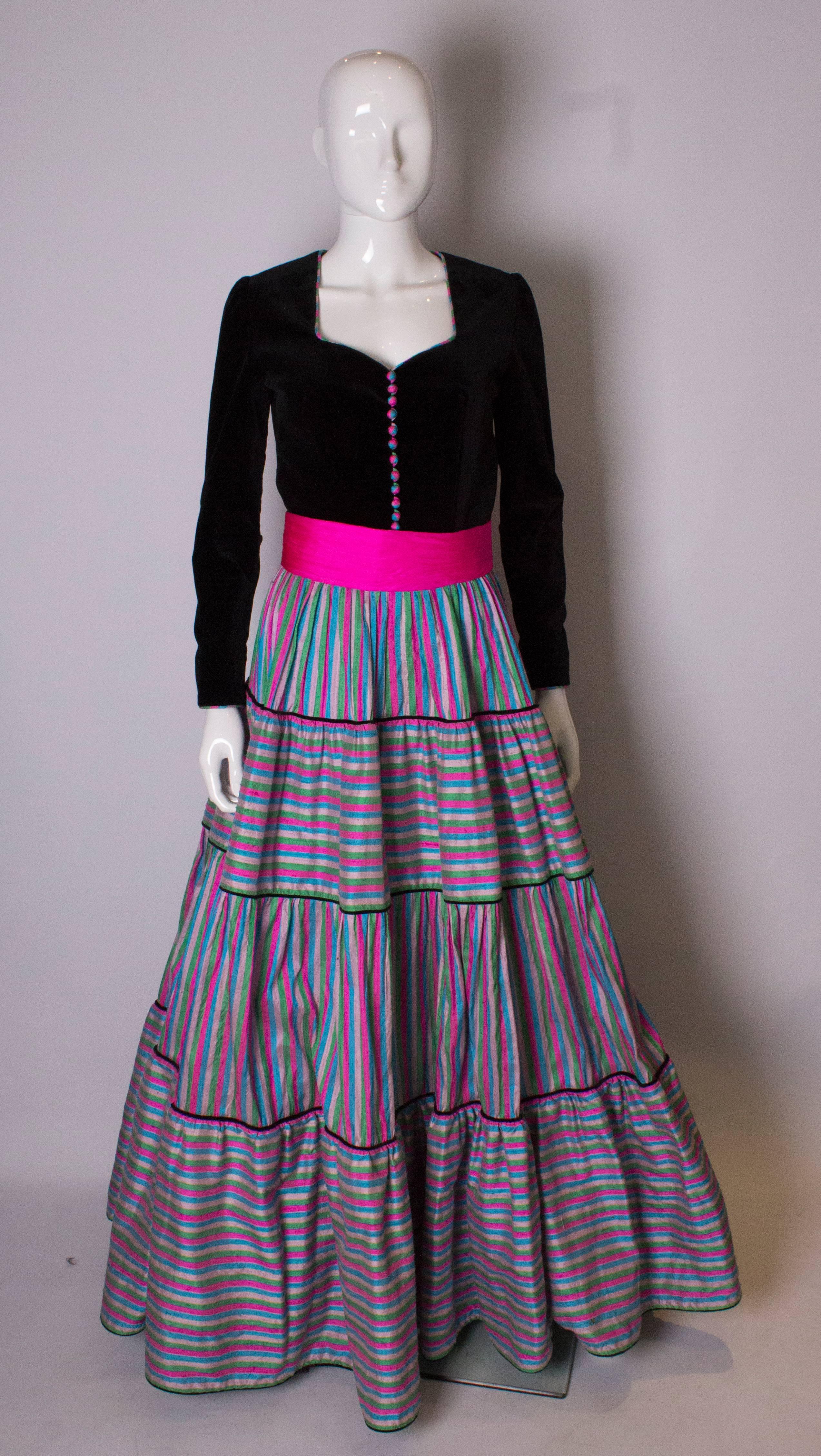 A great gown by Regamus London. The gown has a black velvet top half with a sweetheart neckline. It has a full skirt, with silk tiers of horizontal and vertical stripe silk. It has a net underskirt which is edged in coloured silk,and a central back