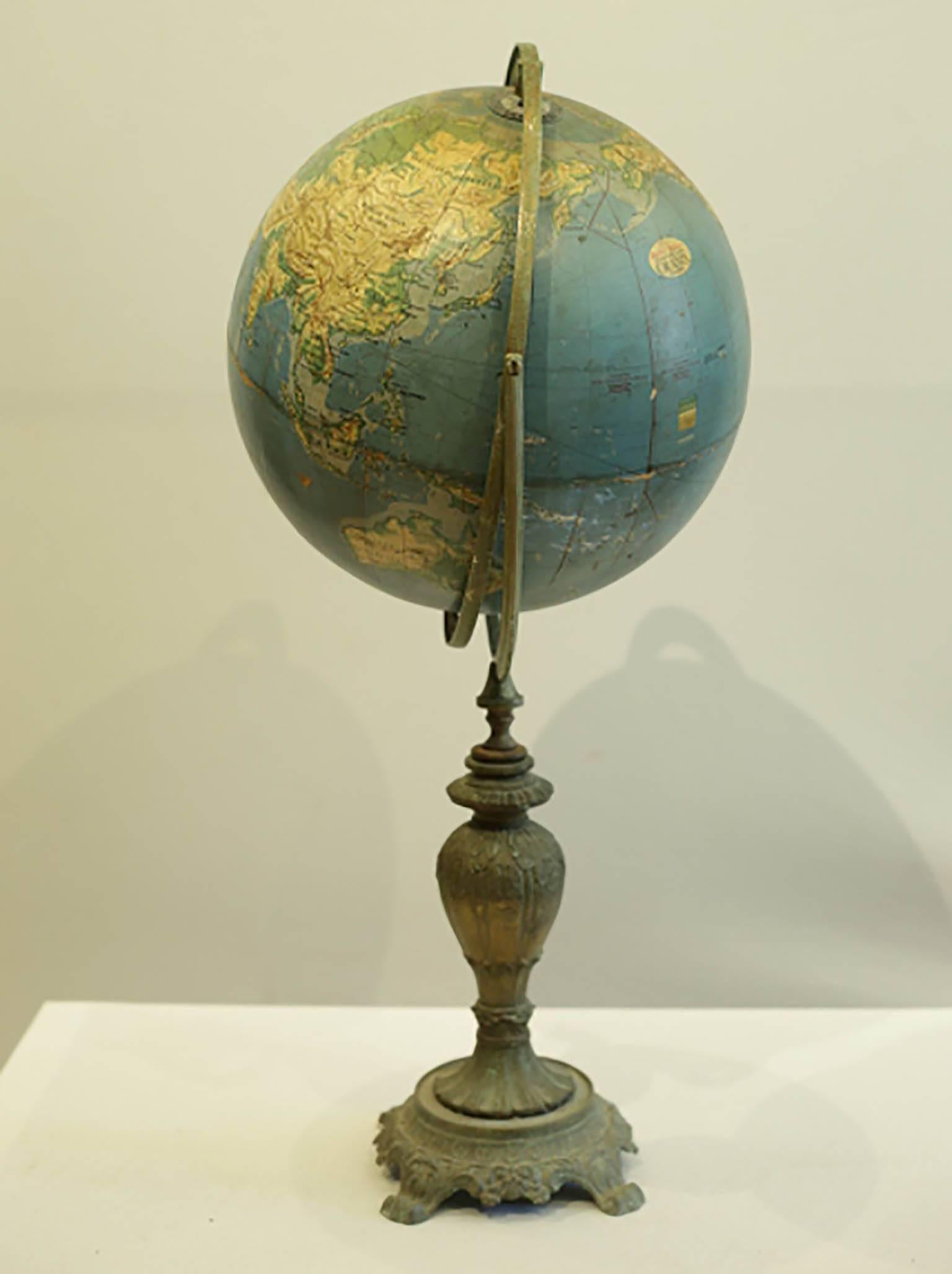 Large topographic globe by Grams with patinated metal bracket and base. 

Condition:
The globe is slightly wobbly from the middle section up.
The globe lifts off of the stand leaving a long stem. There appears to be a piece missing in that area