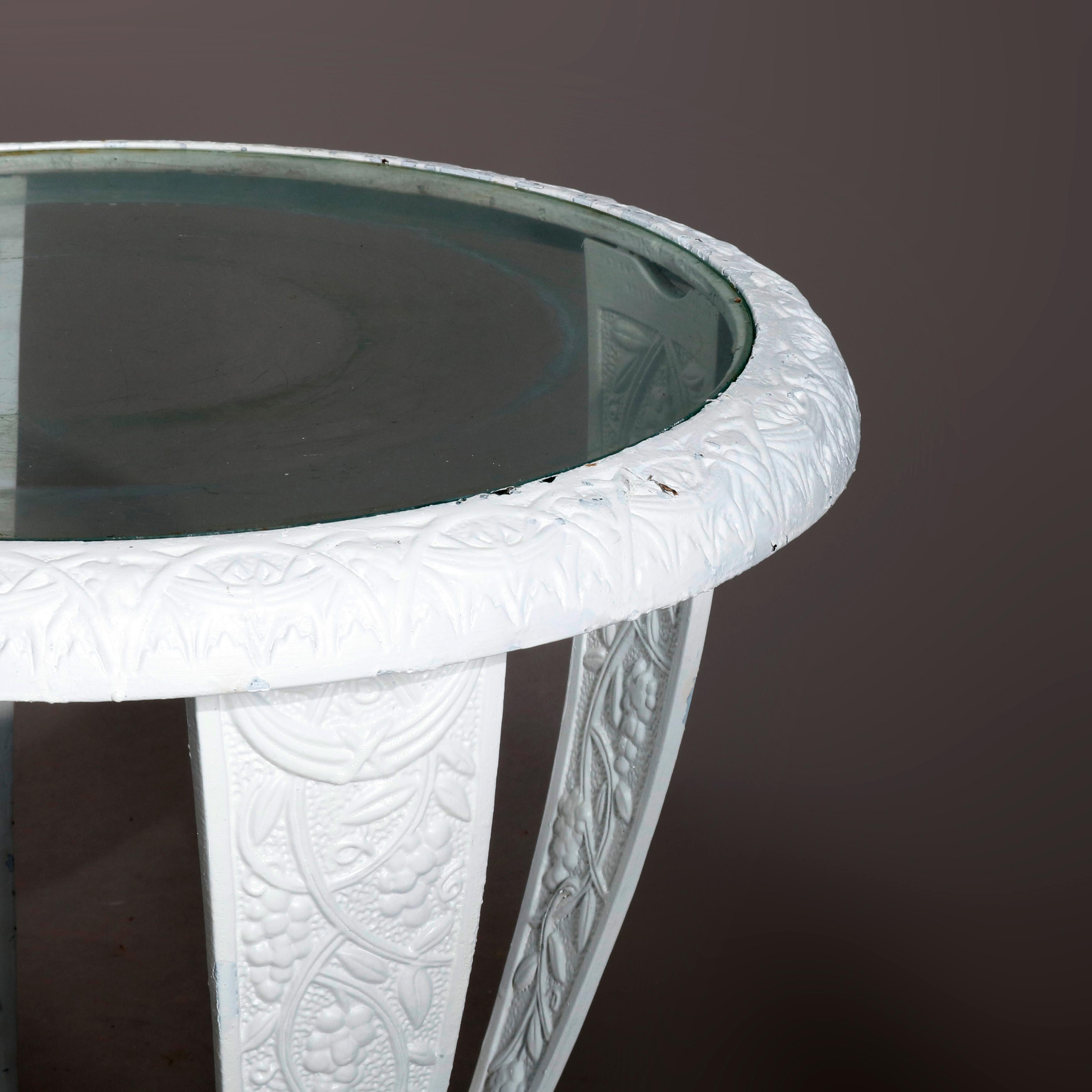 A vintage side table offers glass top surmounting balloon form cast iron base having four legs with grape and leaf pattern in relief, raised on stylized paw feet, whit painted, circa 1940

Measures: 20