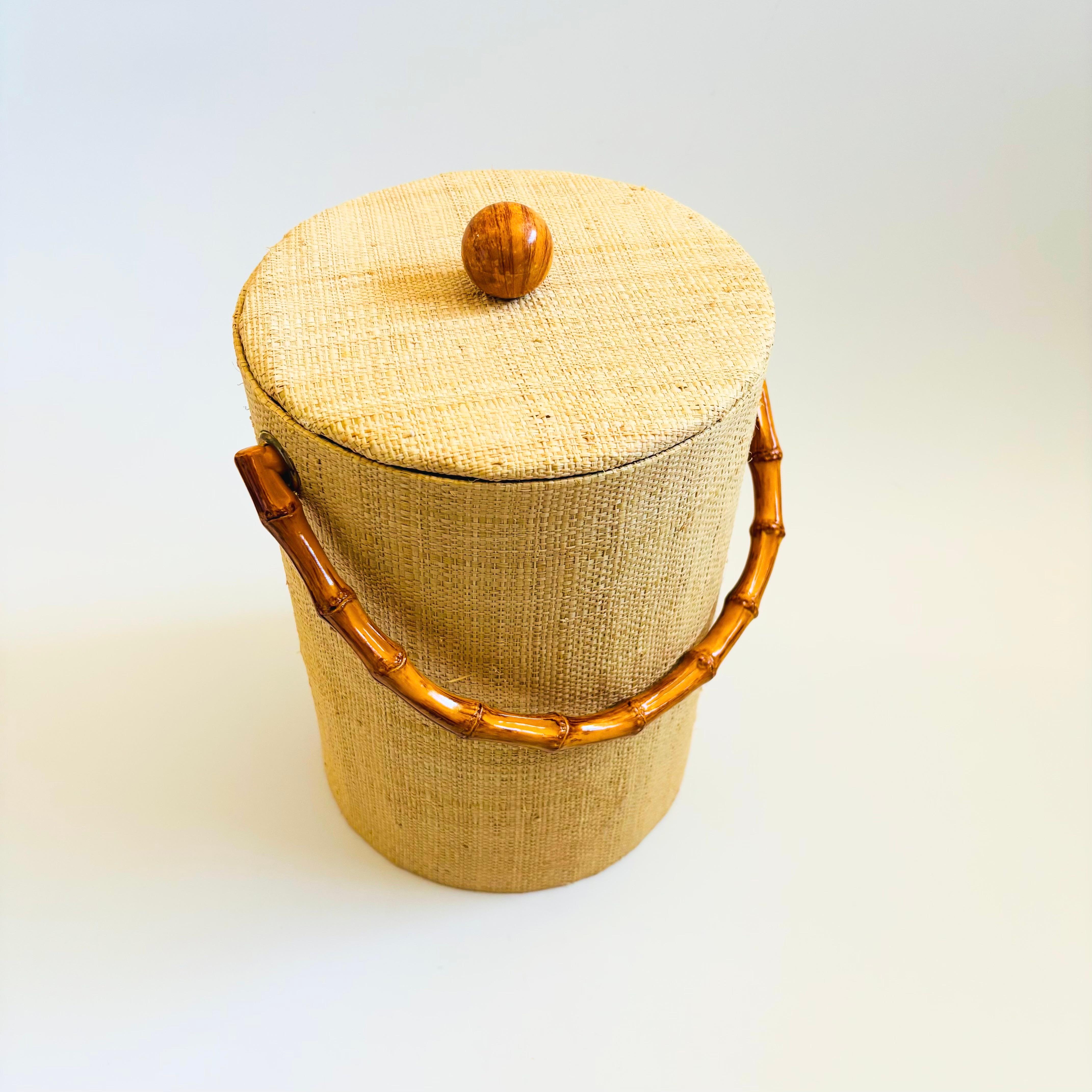 A mid century vintage ice bucket. Wrapped in light tan grasscloth with a wood knob on top and a bamboo handle. Clean white plastic interior.

