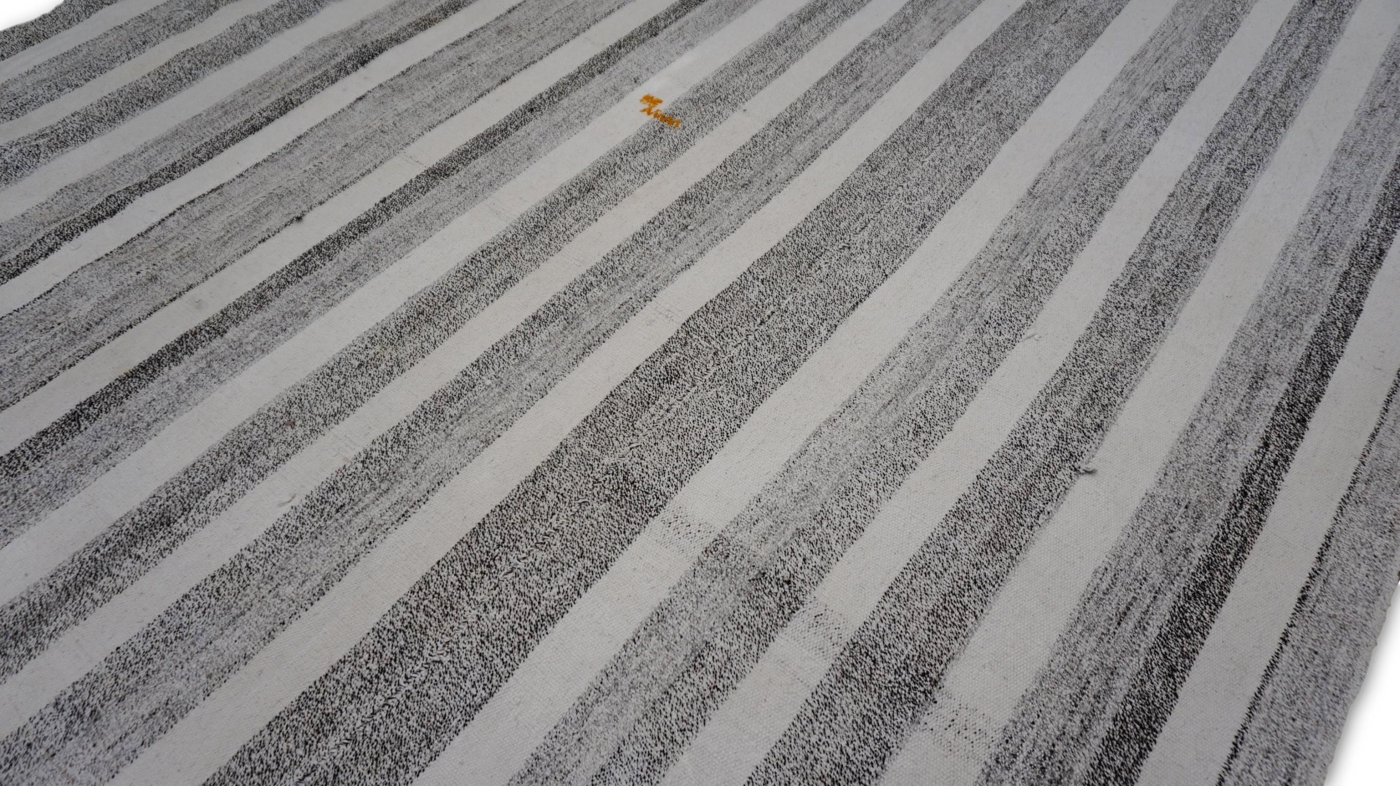 Esta alfombra de lana tejida a mano es una pieza extraordinaria que encarna maravillosamente el minimalismo moderno con un diseño a rayas atemporal. Con rayas verticales alternas en gris, crudo y marfil, la alfombra crea una estética limpia y