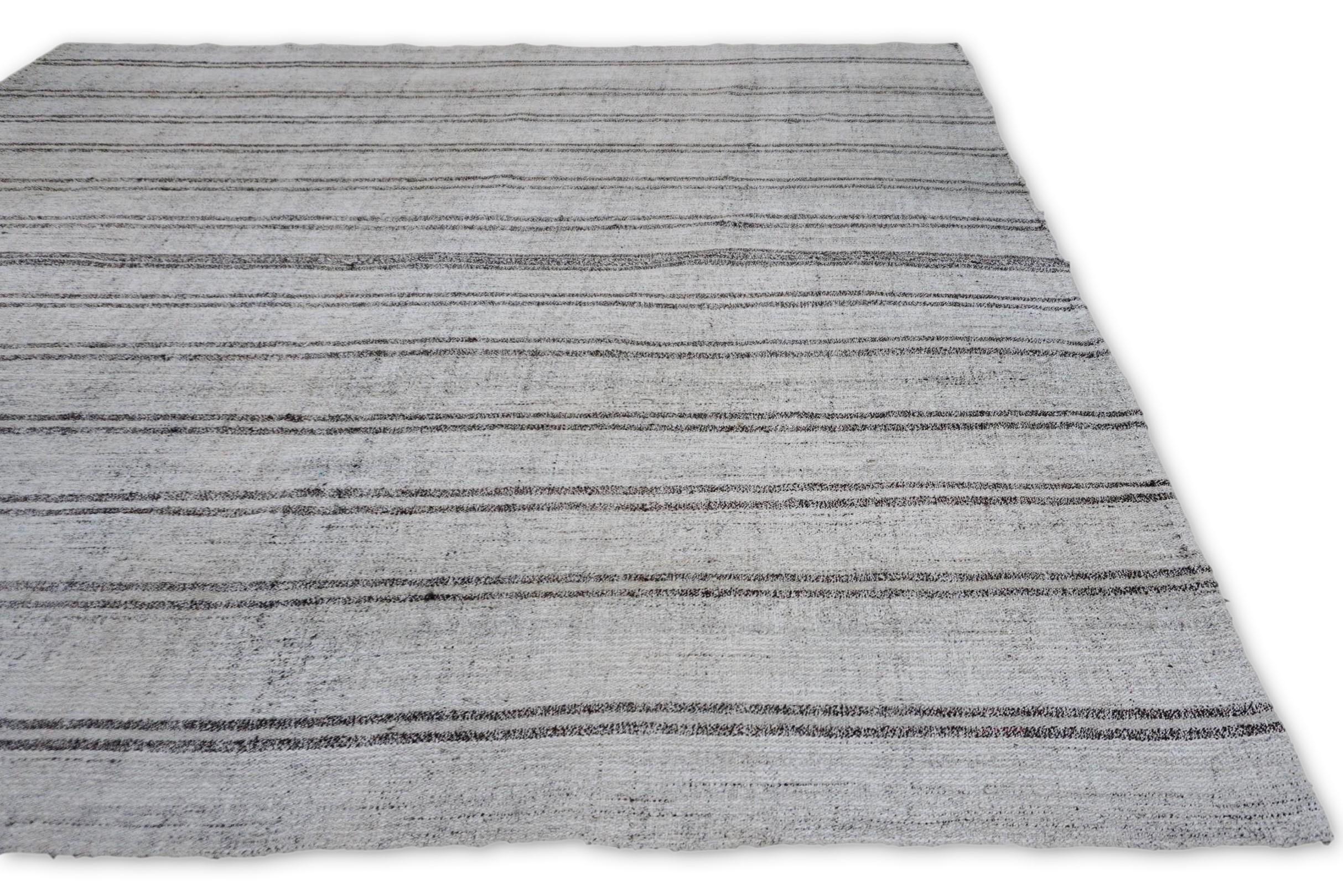 Questo tappeto kilim in lana esemplifica l'estetica minimalista moderna con il suo raffinato motivo a strisce verticali nei toni del grigio, del greige e dell'avorio. Le sottili variazioni nello spessore e nella spaziatura delle linee aggiungono una