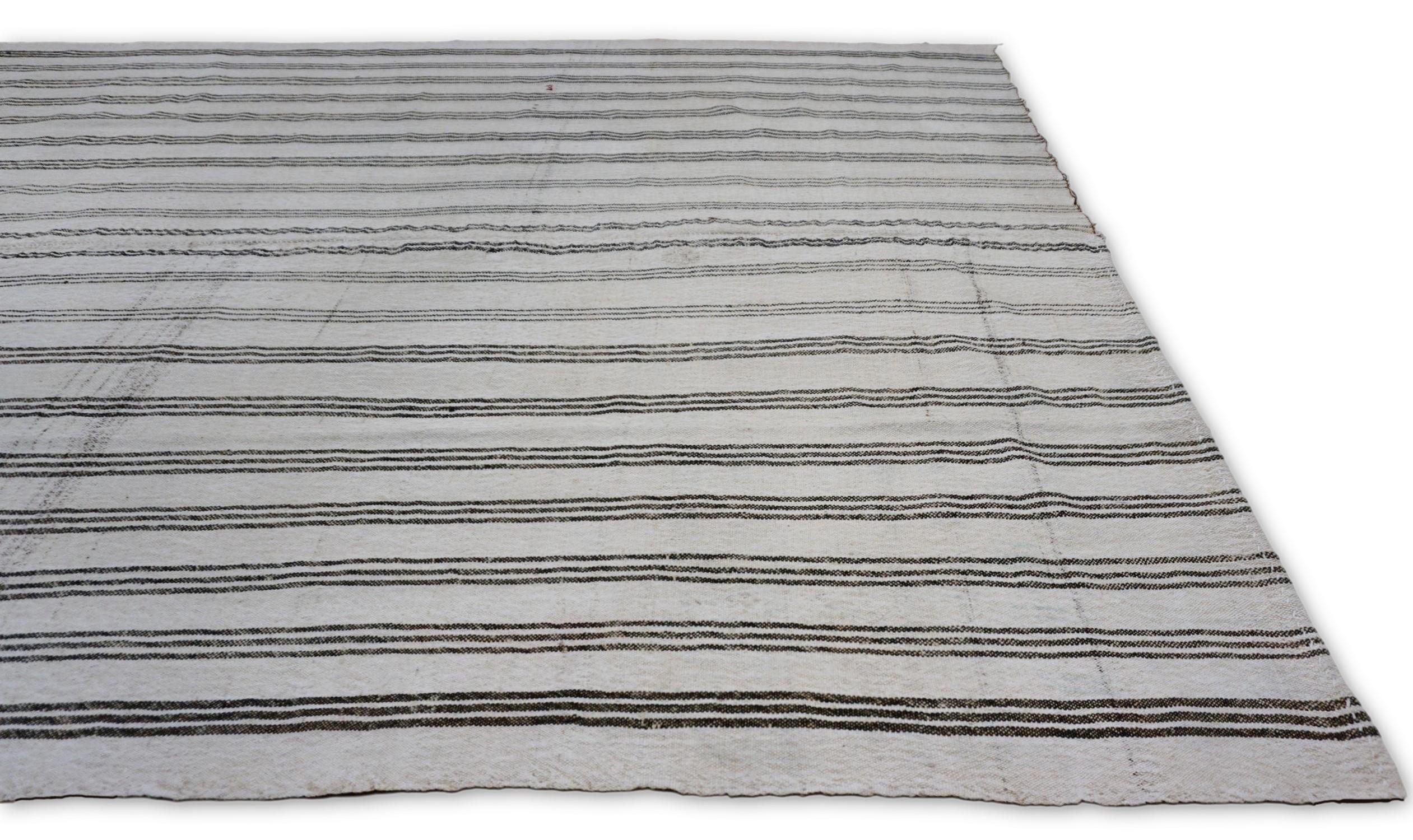 This wool kilim showcases a modern minimalist design with classic vertical stripes in gray, greige and ivory. The subtle variations in line thickness and handwoven texture give the piece an artisanal quality while maintaining a sleek, contemporary