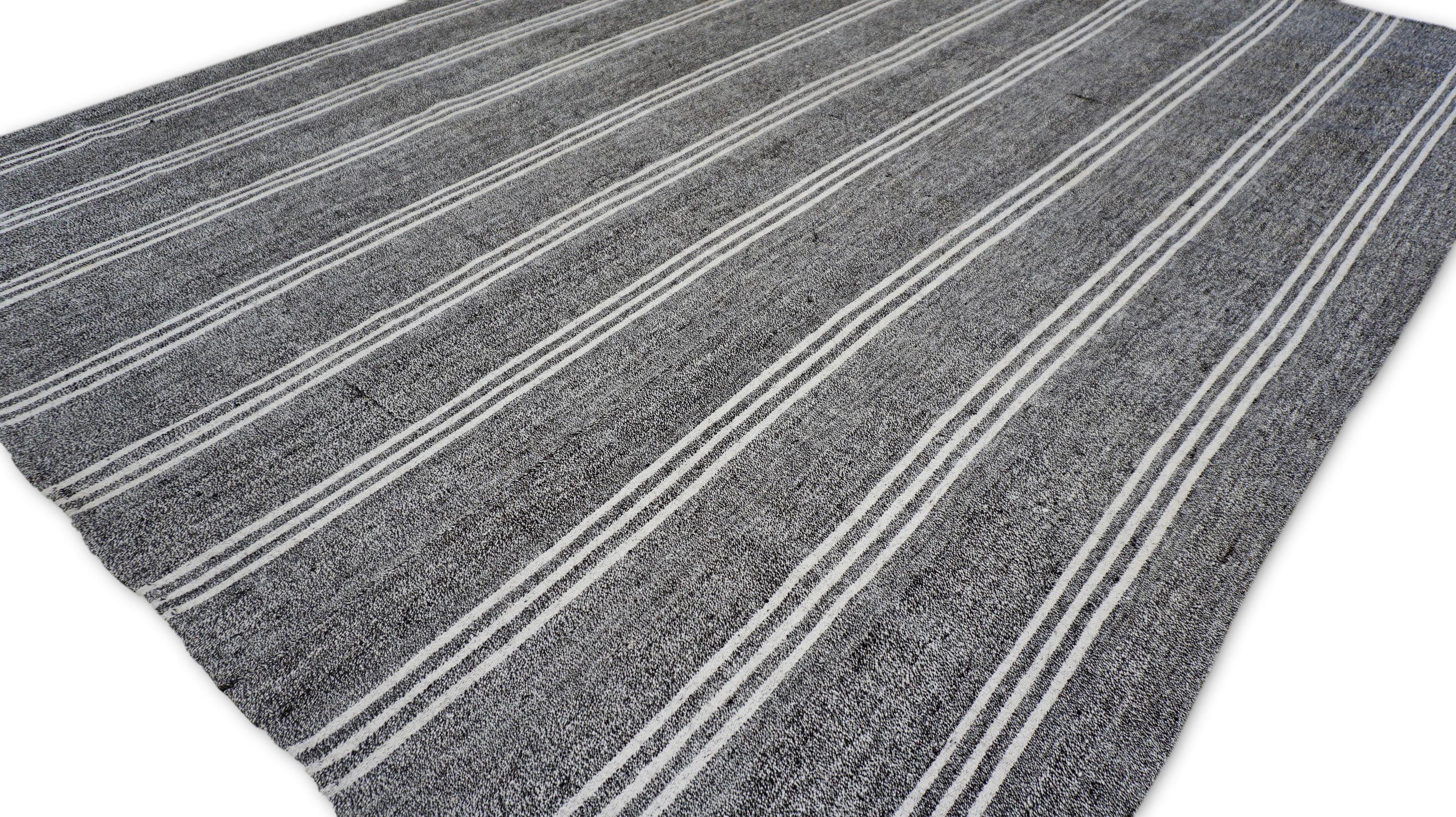 This handwoven wool flatweave is a vintage kilim rug, crafted using traditional flatweaving techniques native to nomadic region. Dating to the 20th century (circa 1960), this showcases a timeless striped pattern composed of natural white and gray