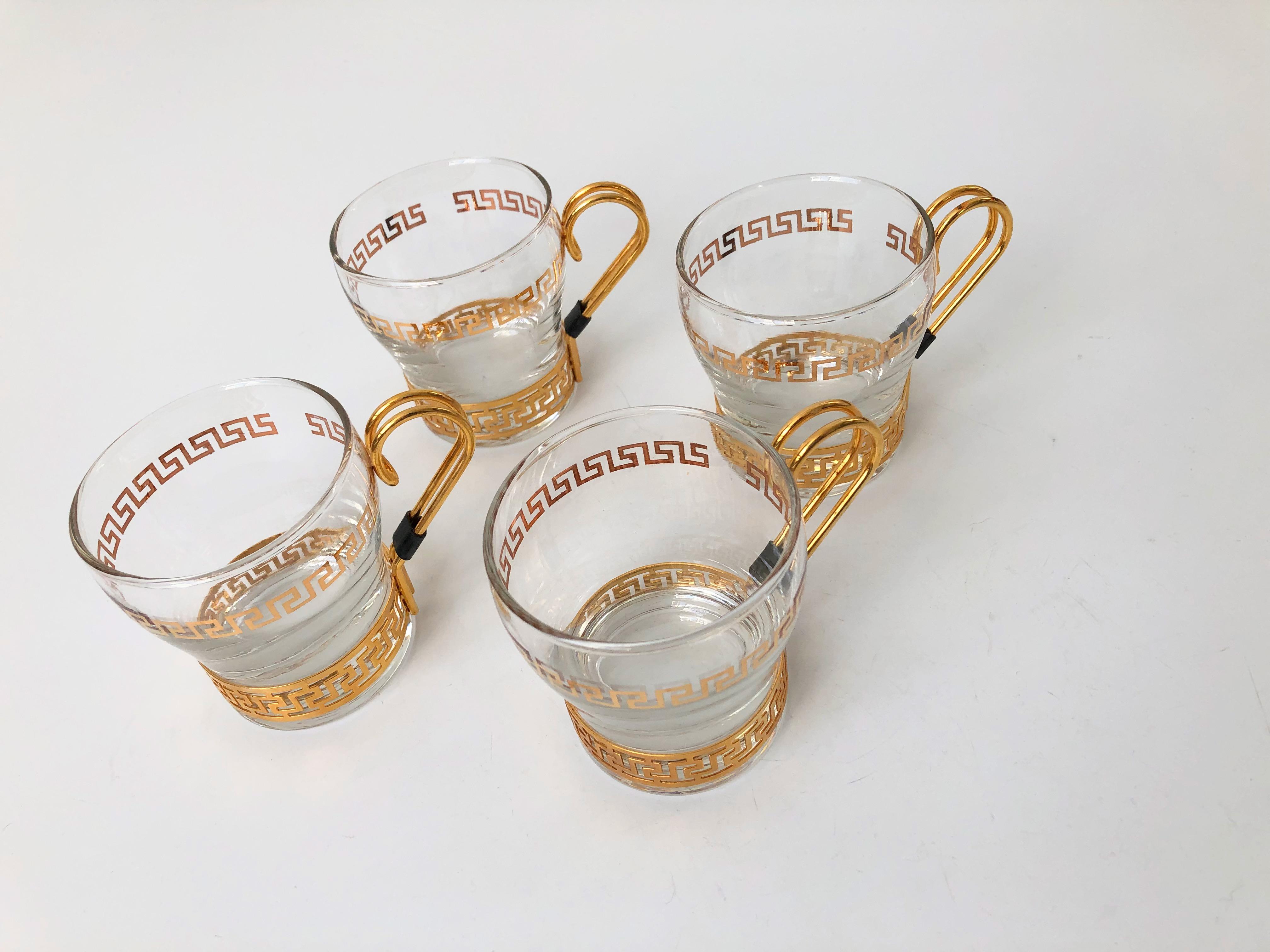 Un ensemble de 4 verres courts vintage avec des supports en laiton. Un motif de clé grecque dorée entoure chaque verre avec un support en laiton assorti. Parfait pour les boissons chaudes ou froides. Fabriqué par Libbey. 2 Sets de 4 sont