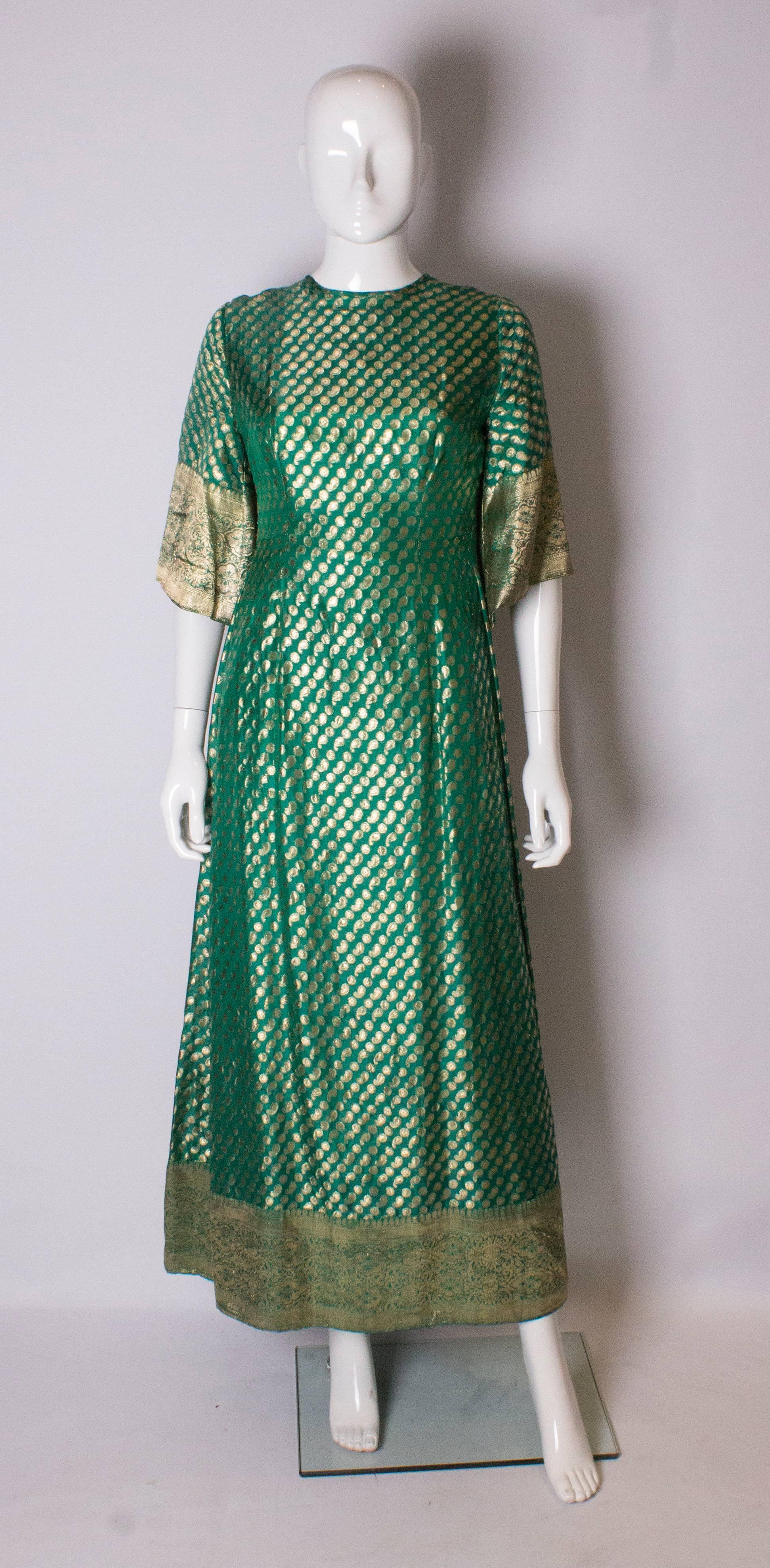 A stunning Indian silk gown in green and gold. The dress has a round neckline at the front, and a v neckline at the back with gathering.  It has elbow length sleeves and wide gold detail at the hem.