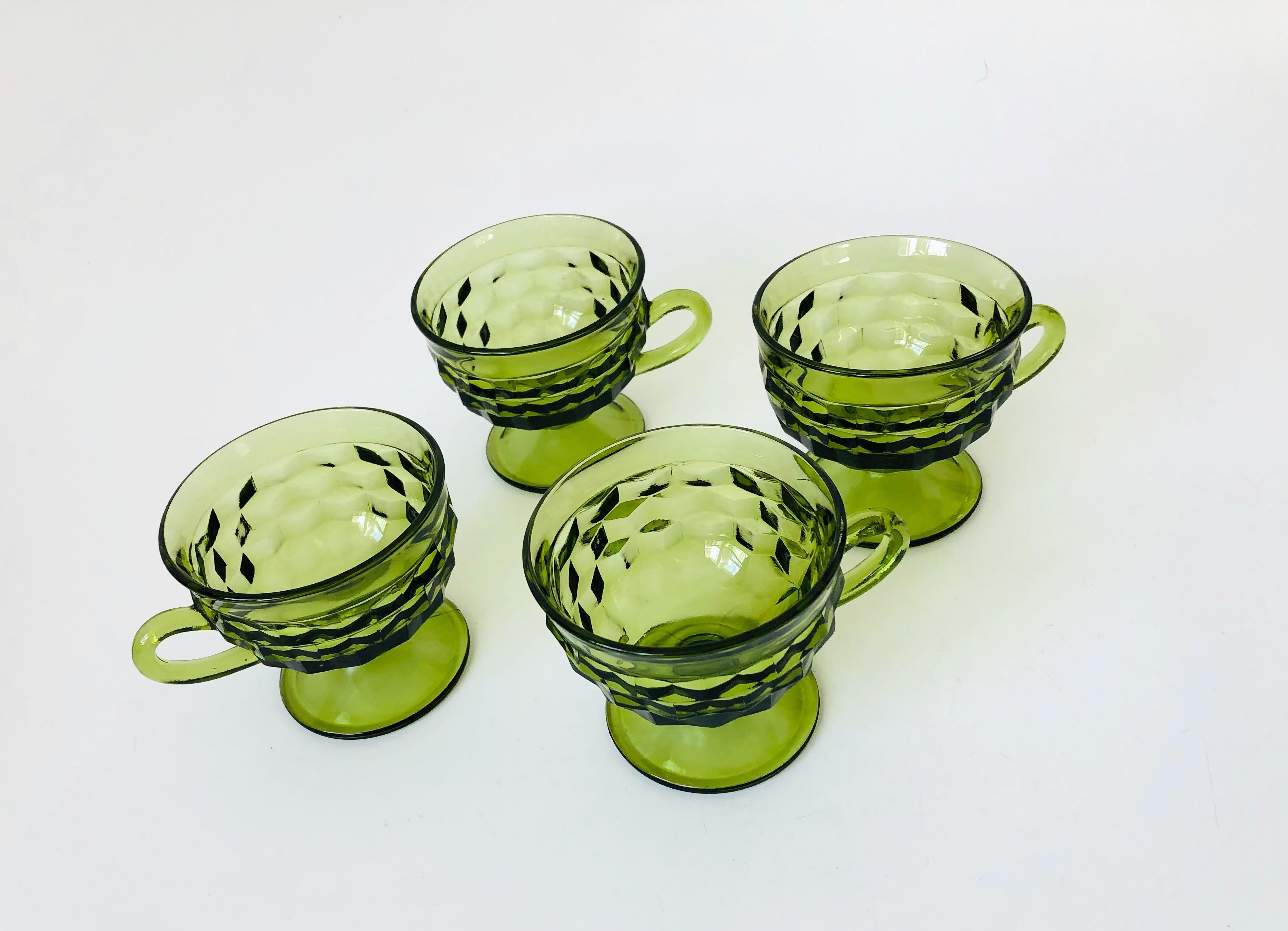 A set of 4 vintage coupe glasses with handles. Each with a cubist design in thick green glass. Made in the Whitehall pattern by Indiana Glass. Perfect for wine or champagne. Smooth interiors.
   