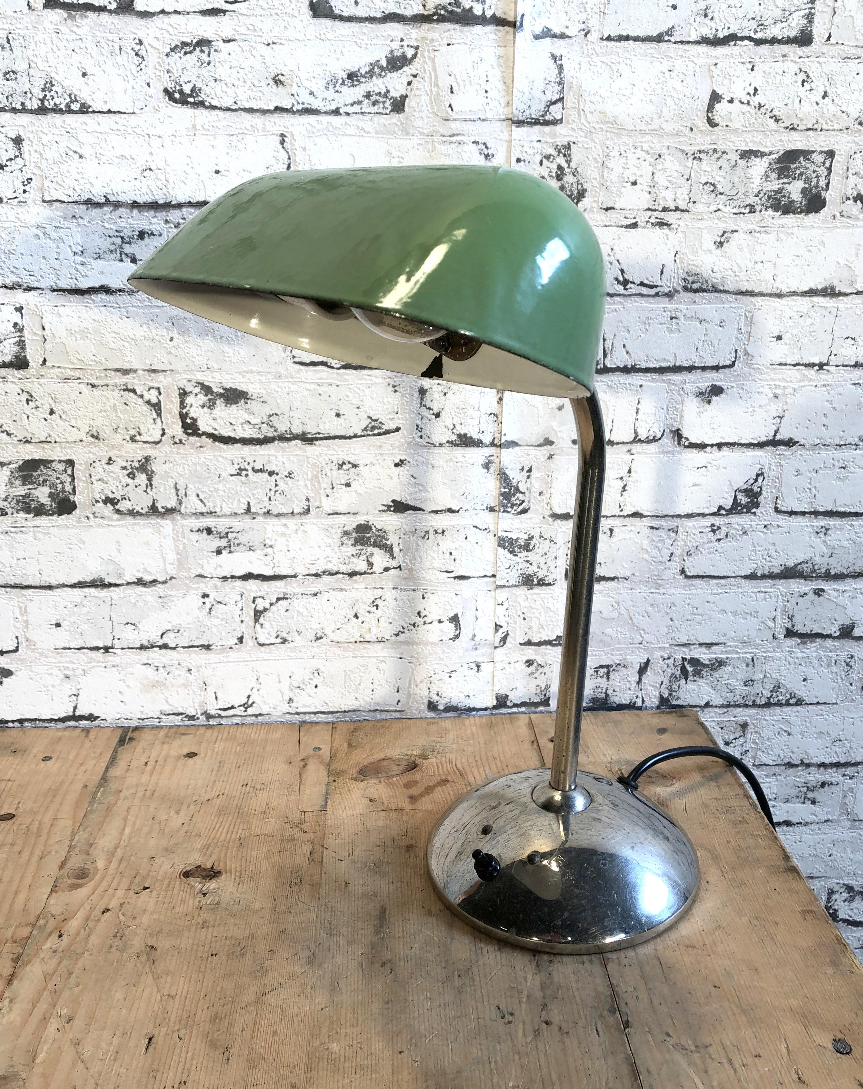 This green table lamp was made during the 1930s. It features a green enamel shade with a white enamel interior and a chrome plated iron base with two adjustable joints. The new porcelain socket takes an E 27 bulb. New wire. Fully