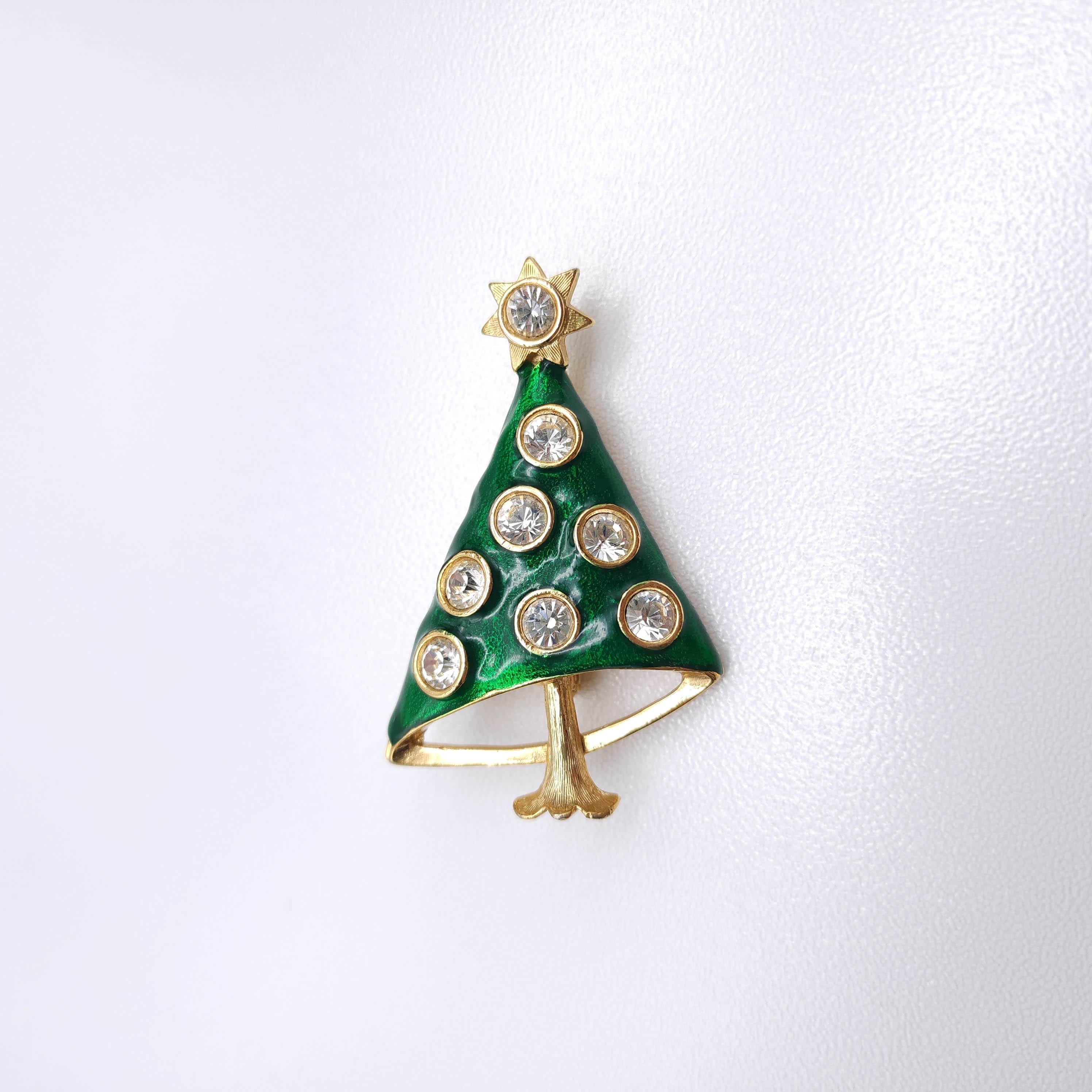 A stylized Christmas tree design, crafted in green enamel and adorned with seven bezel-set rhinestone ornaments. 

The tree's modern, triangular shape is accented with a golden star at the top, set with an additional centerpiece crystal for added