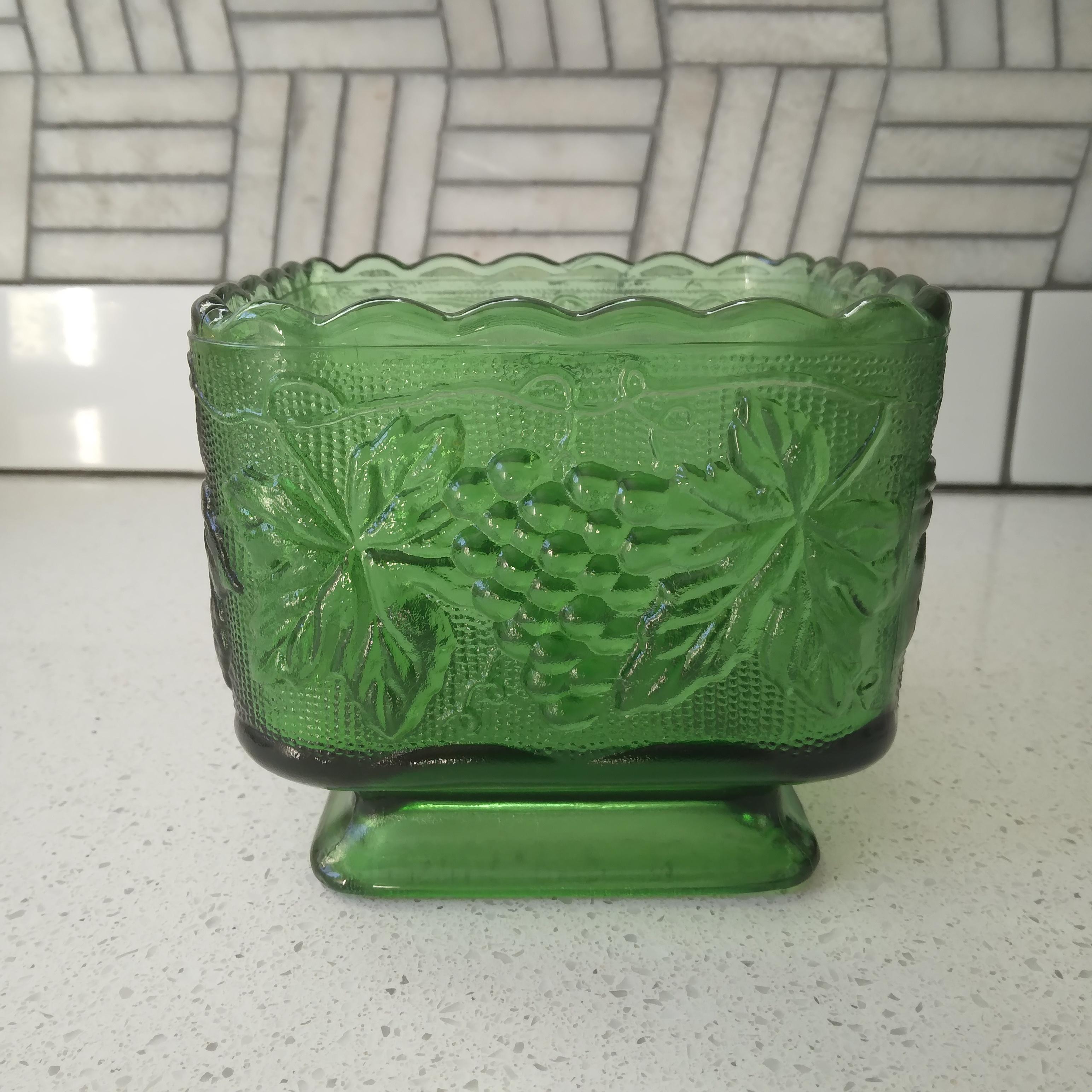 Sturdy and beautiful, we love the vibrant green tones of this vintage bowl. 

This glass piece features an beautiful grapvine design with a scalloped top edge and small footed pedestal. The bold bottle coloring and thick walled glass make this a
