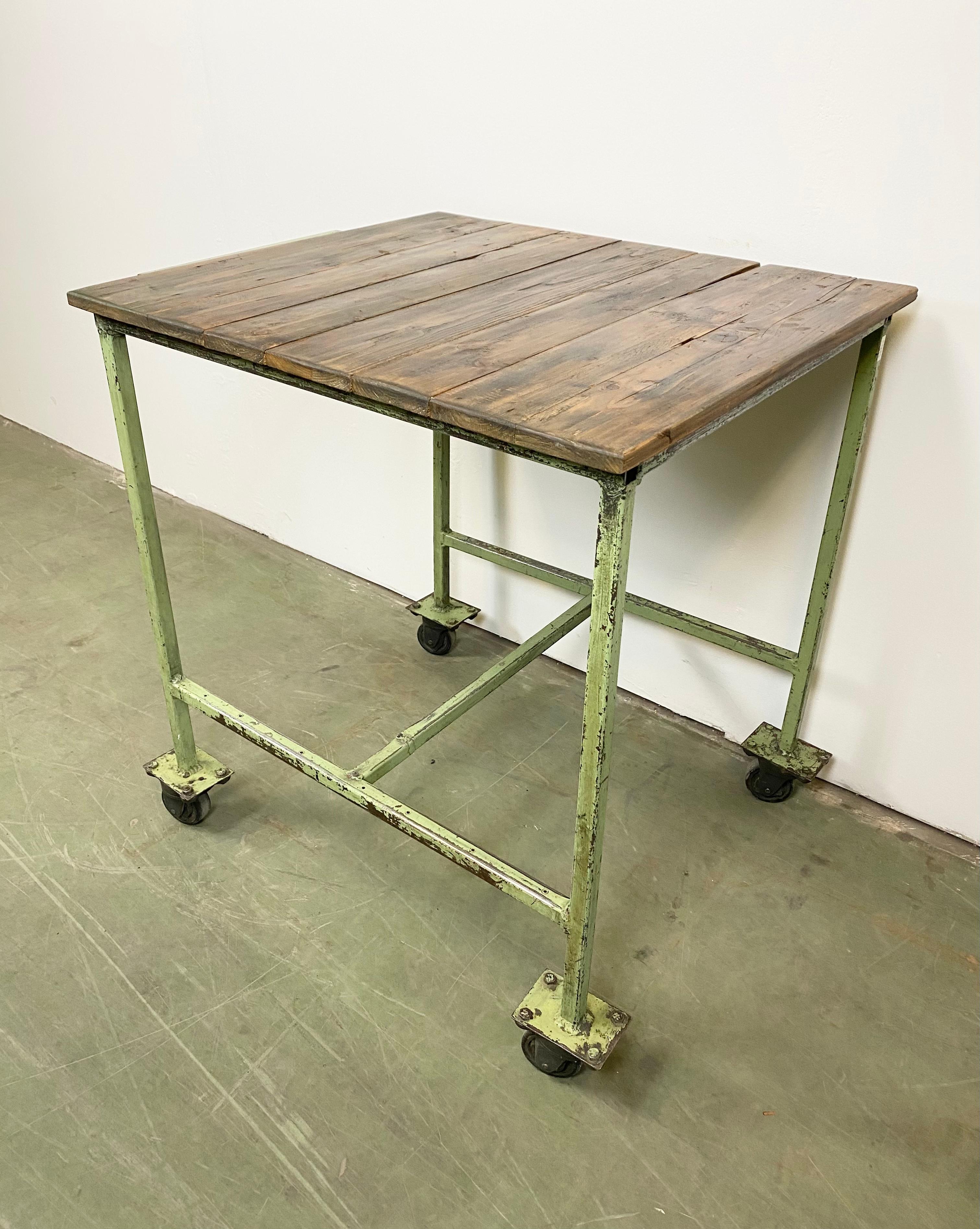 Industrial trolley from 1960s. It features an iron construction with four wheels and wooden top. Good vintage condition. Weight: 38 kg.