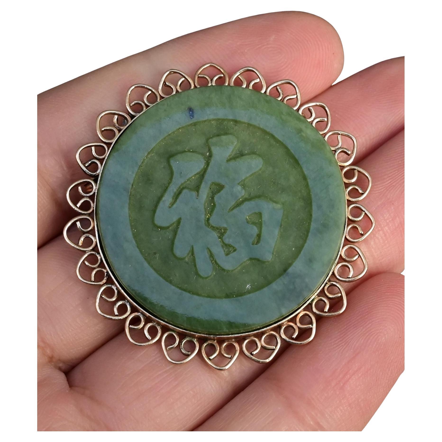 This elegant vintage green jade pendant brooch showcases a finely carved “Fu” (福) character, symbolizing blessings and good fortune. The jade disc is encircled by an intricate 14K yellow gold filigree frame, adding a delicate and timeless touch.