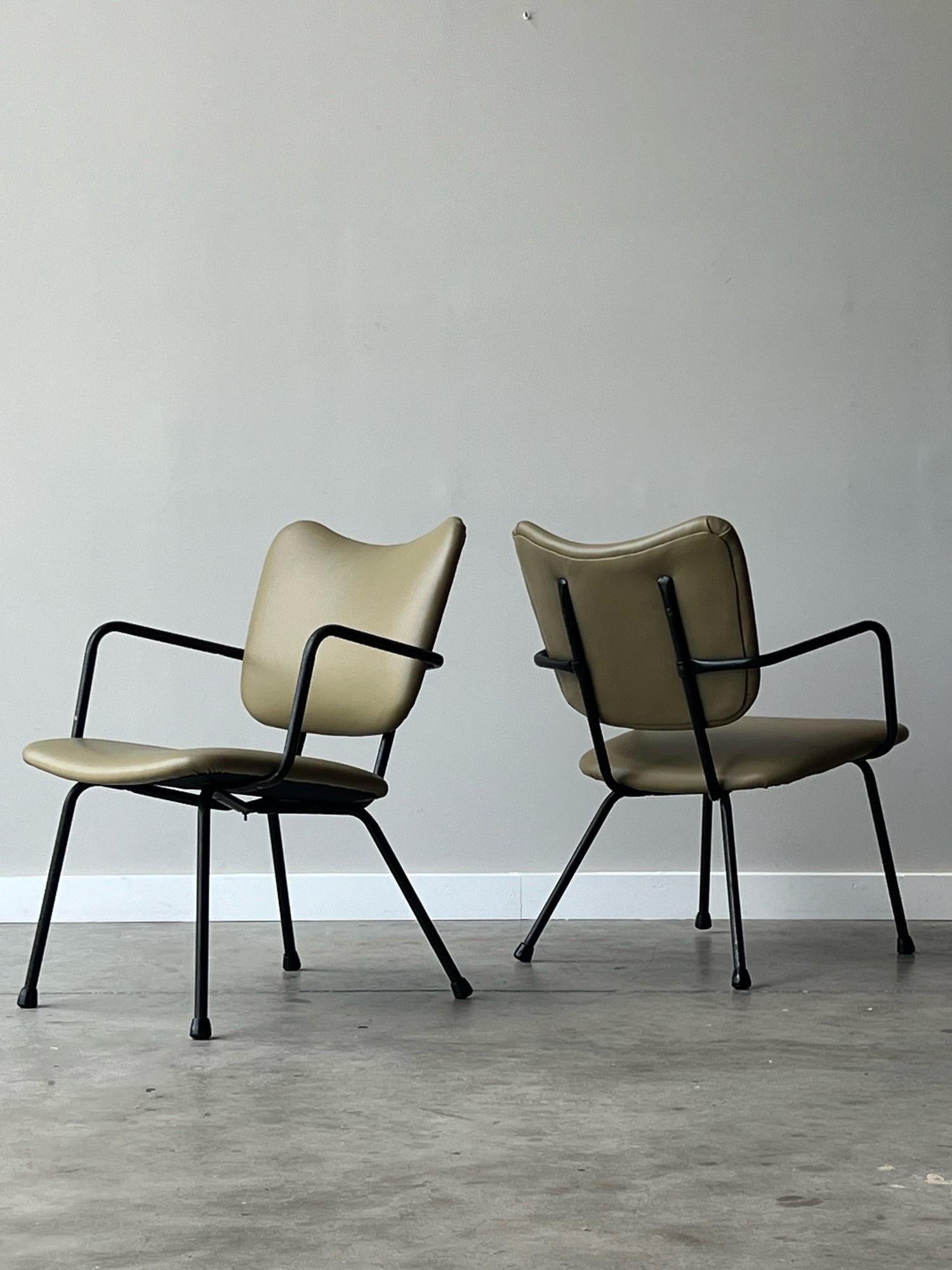 Vintage black metal frame armchairs, made circa 1950s. This pair has a smaller footprint, but score major points in style and comfort. The two cushions have been newly reupholstered in green leather. The color of the leather is neutral, natural, and