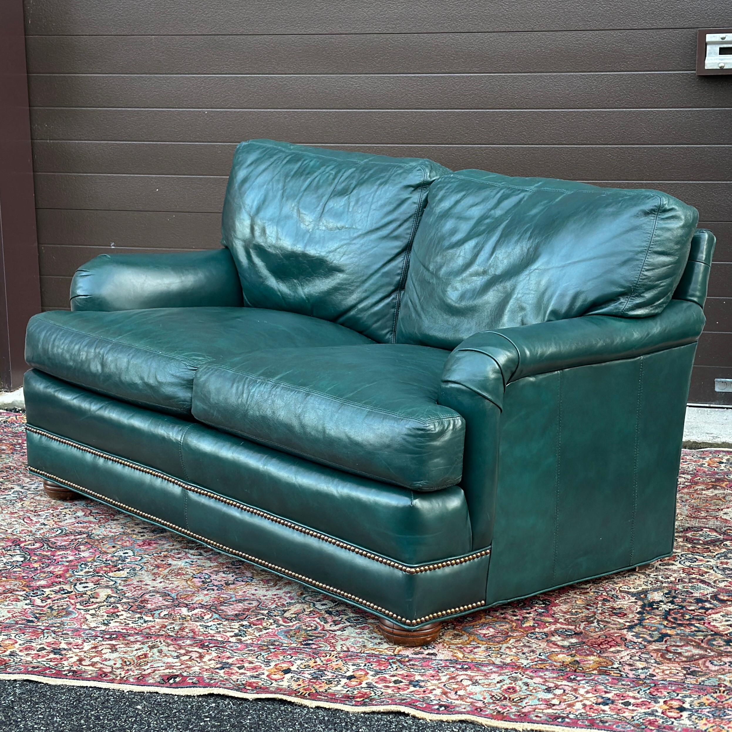 Vintage Green Leather Loveseat With Brass Tack Trim by Hickorycraft with wooden bun feet in the front and square wooden back feet that are hidden. Matching ottoman and lounge chair available at time of listing!